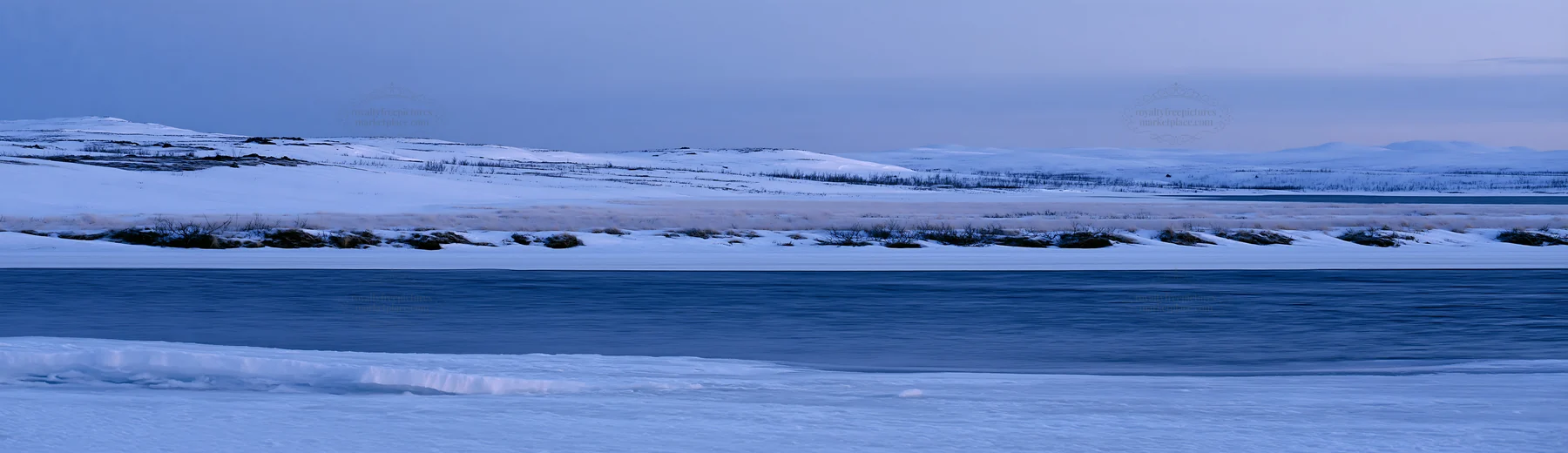 Snowy highland meadow with a frozen river under a blue sky - AI-generated stock image