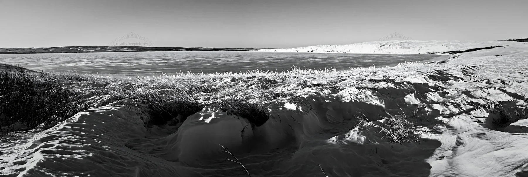 Snowy lakeside meadow with frozen water in winter - AI-generated stock image