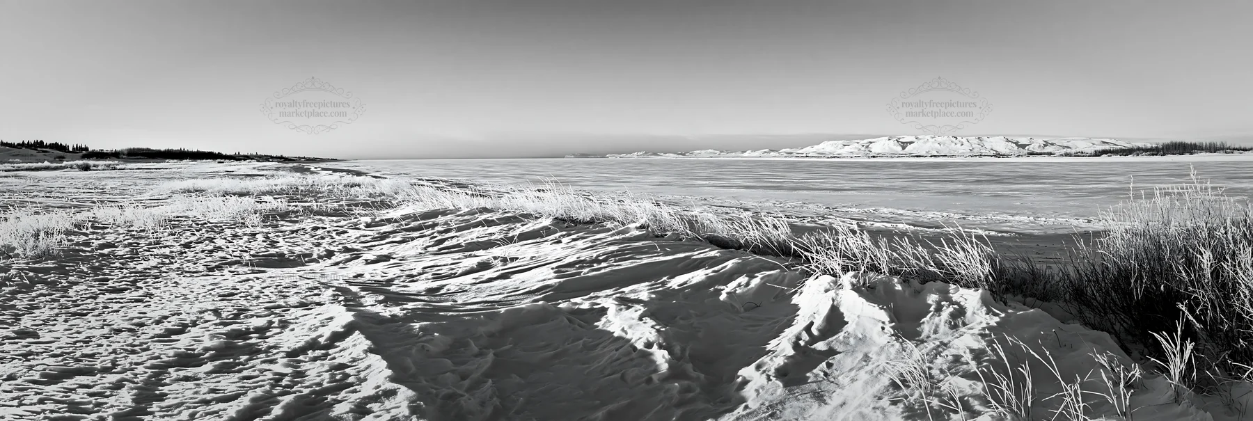 Snowy lakeside meadow with frozen water and distant hills - AI-generated stock image