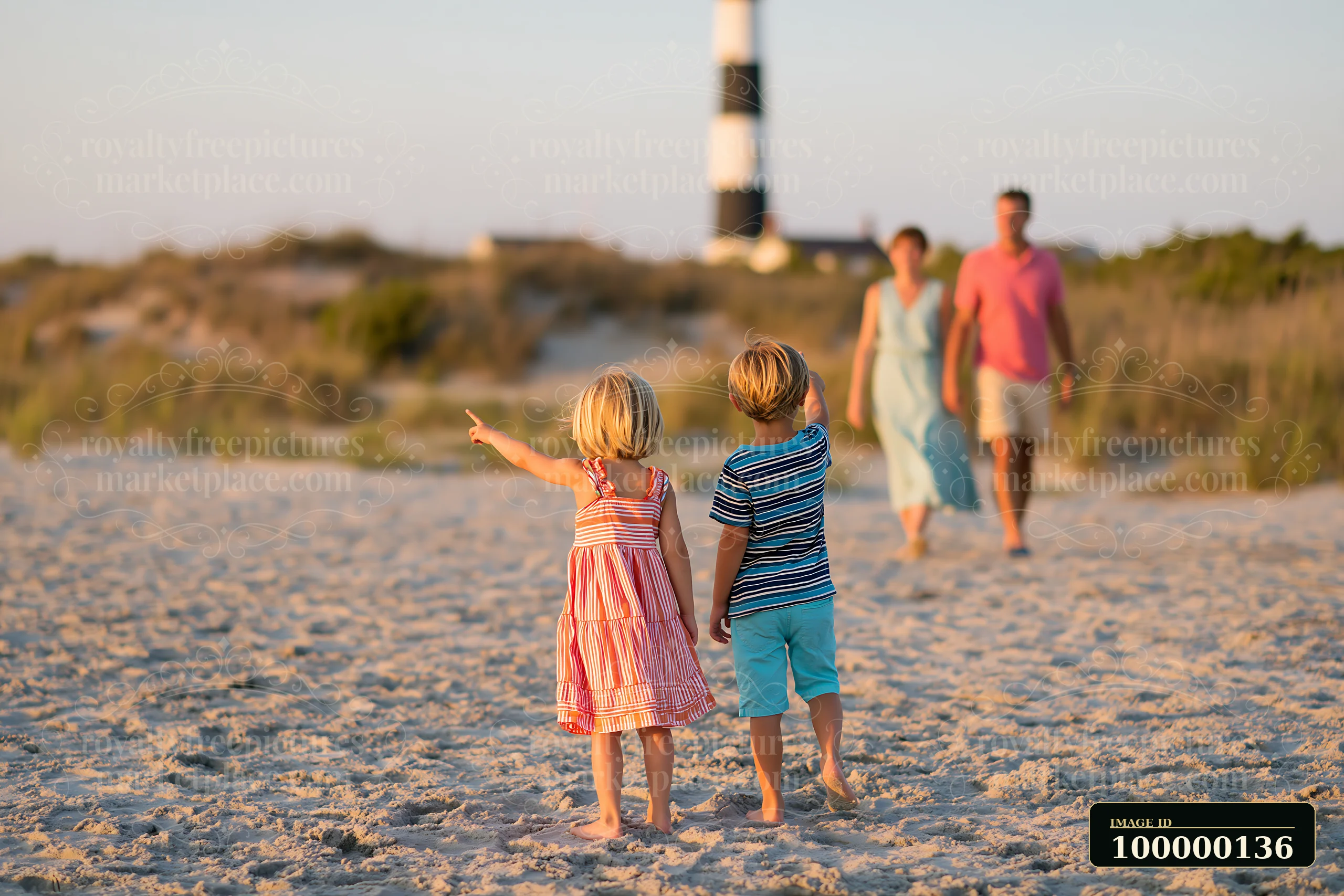 Two children walk across a sandy coastal path toward a lighthouse while two adults follow behind.