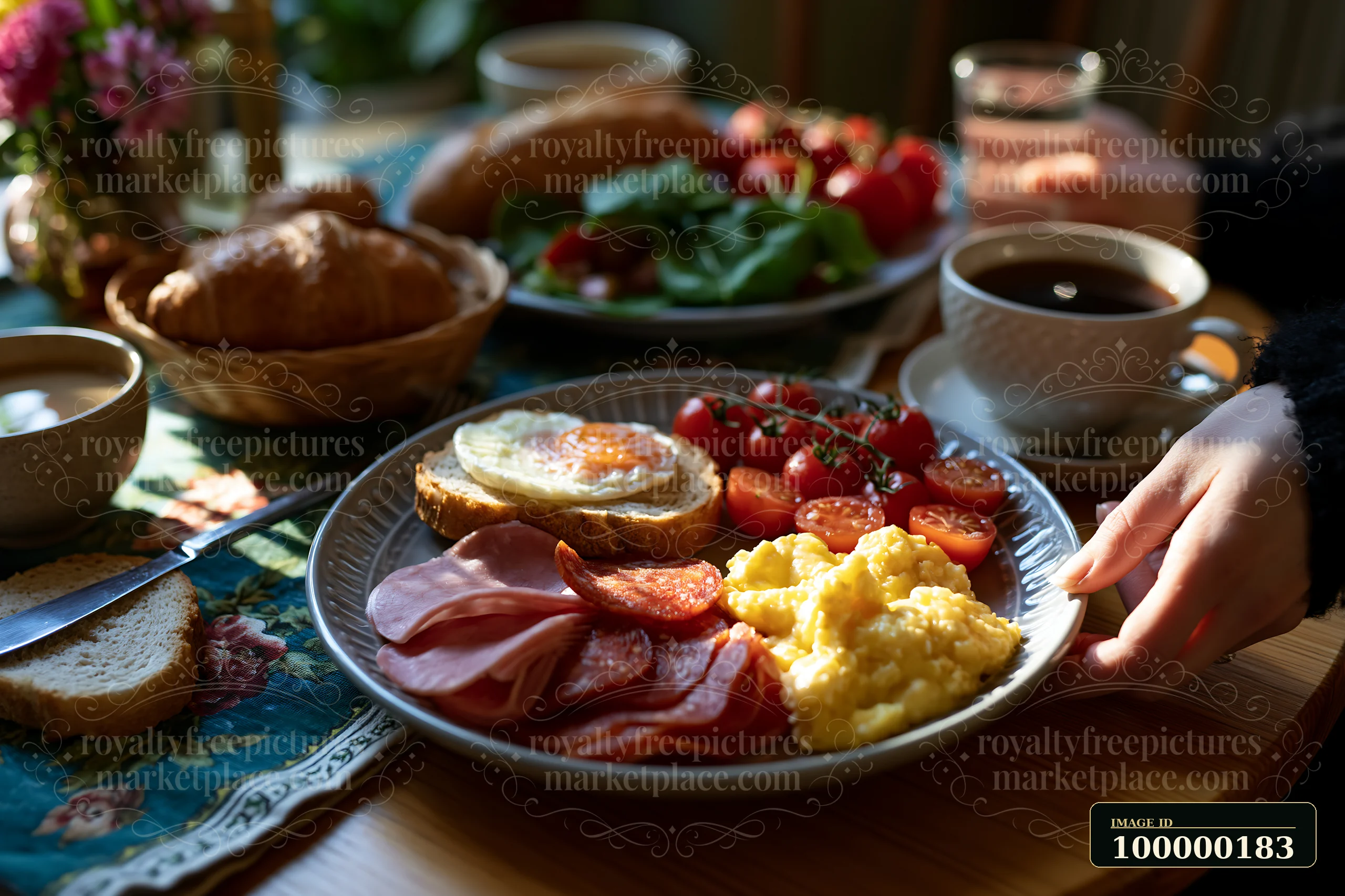 Person serving a breakfast plate with eggs, bacon, ham, tomatoes, toast, and coffee at a warmly lit table.