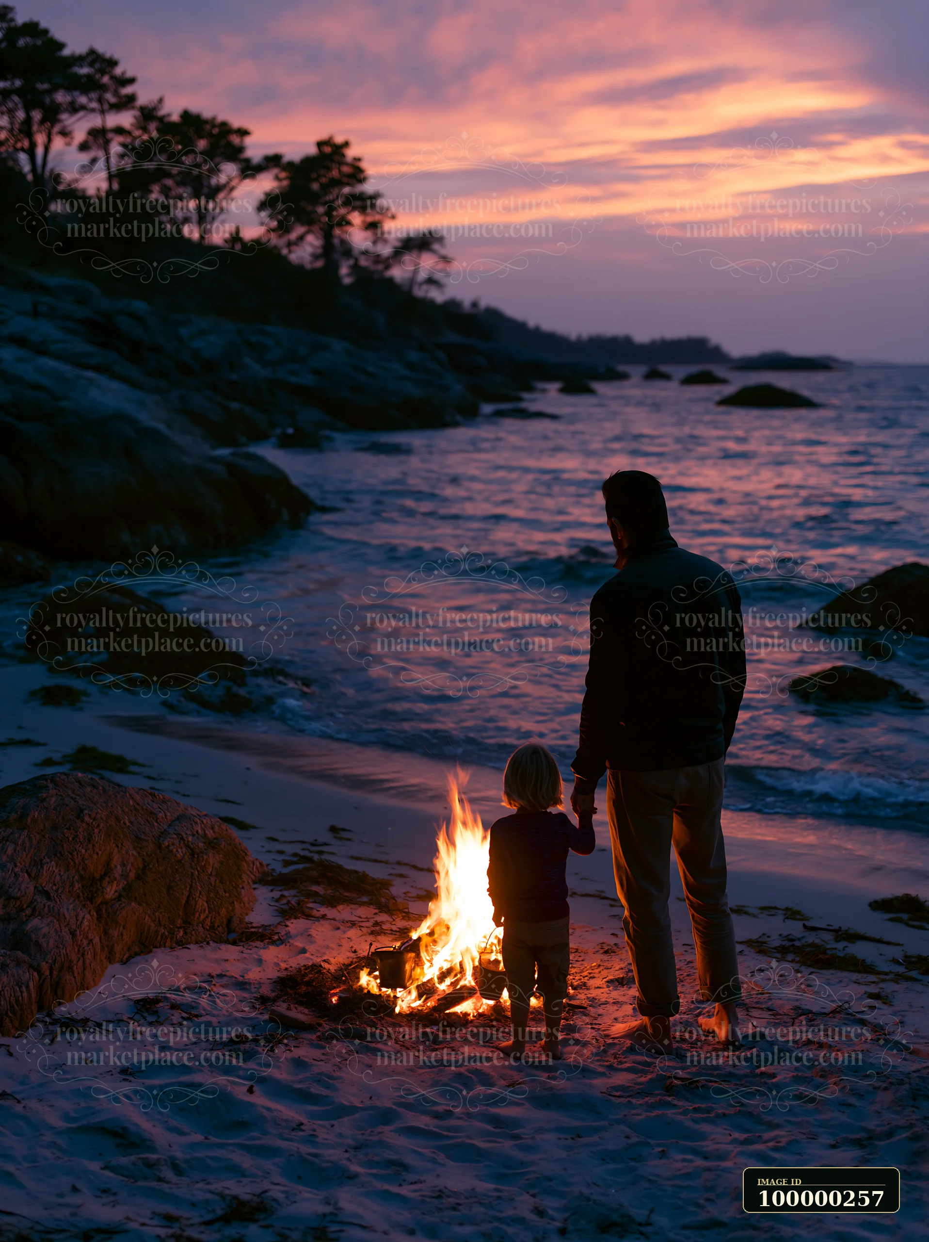 Parent and child stand beside a beach bonfire on a rocky coastline beneath a colorful sunset sky.