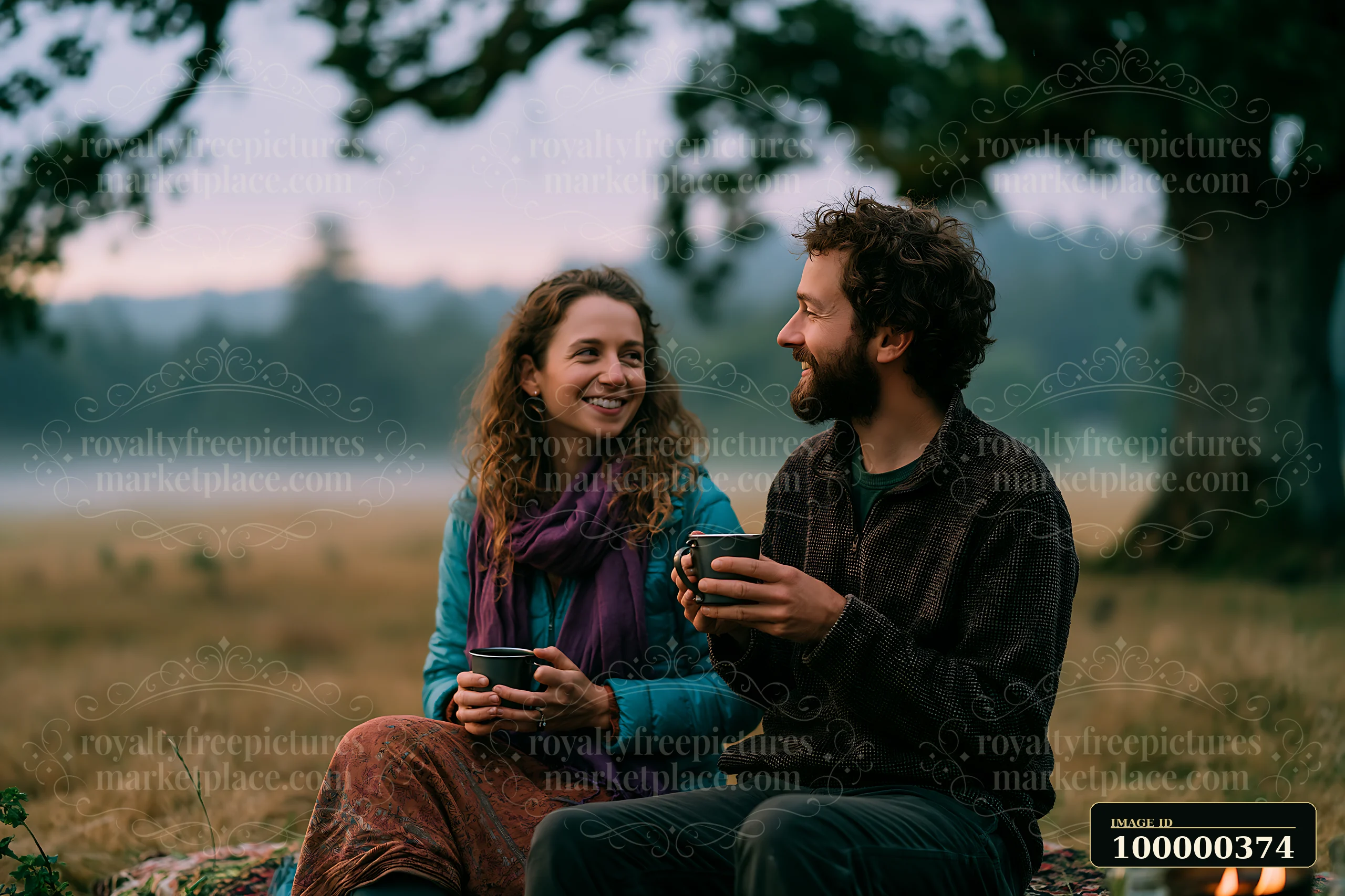 A couple sits on a blanket in a meadow beneath an oak tree, enjoying warm drinks and smiling at each other.