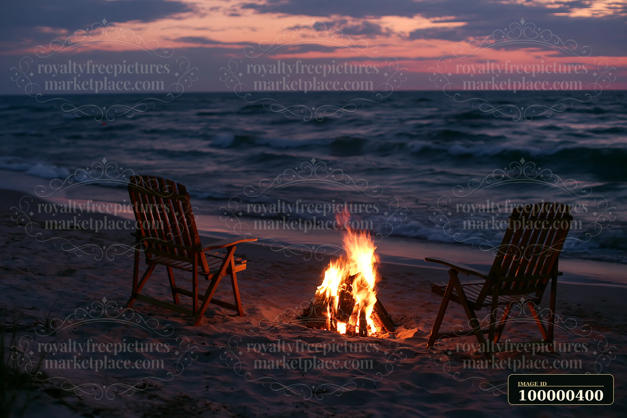 A beach bonfire burns in the sand near the water's edge as two chairs sit empty, framed by waves and a colorful sky at sunset.