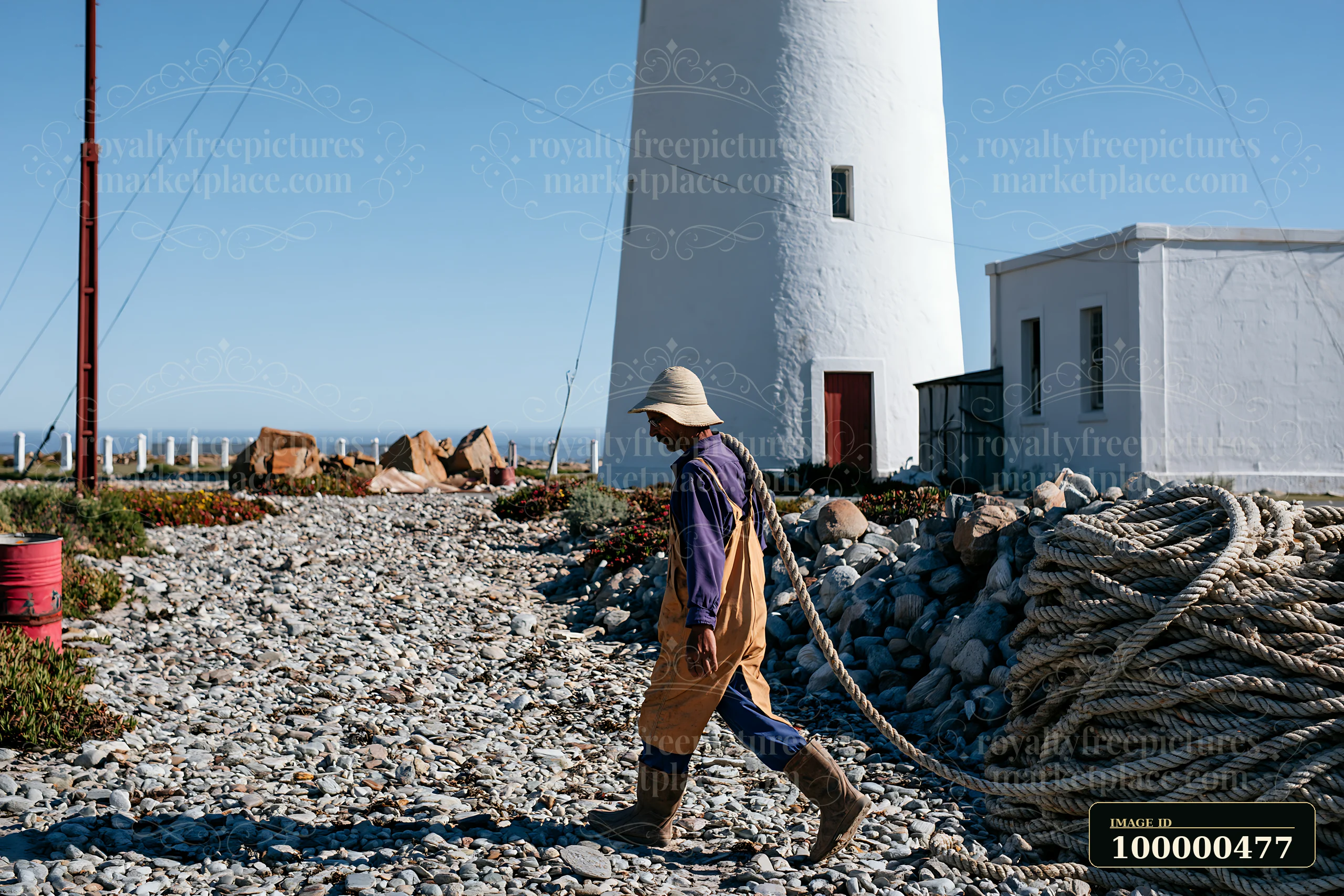 A lighthouse maintenance worker at work walks along a rocky path near the lighthouse, carrying ropes and preparing for tasks to ensure the structure is function