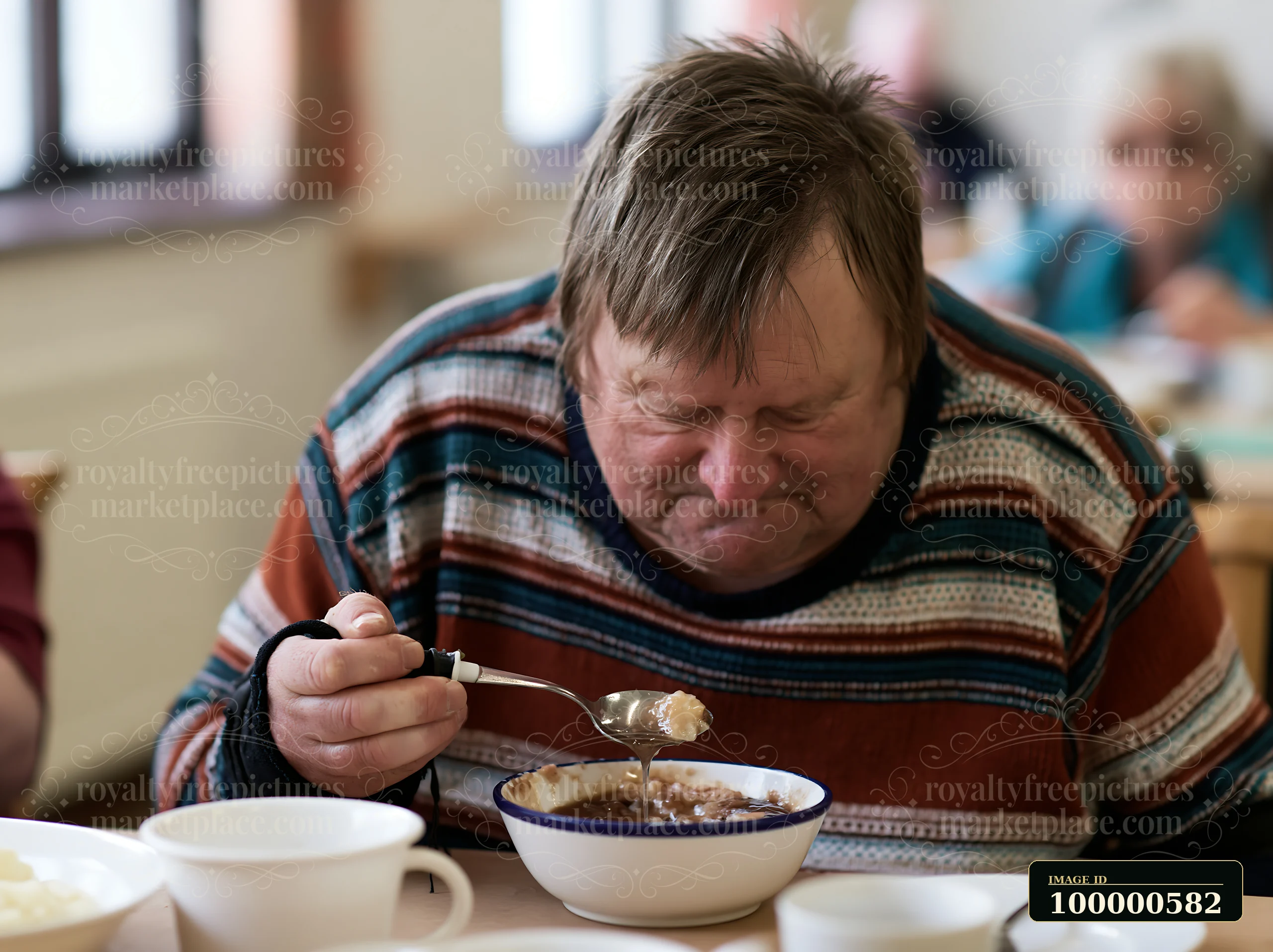 A man focuses on his bowl while eating at a community dining hall.
