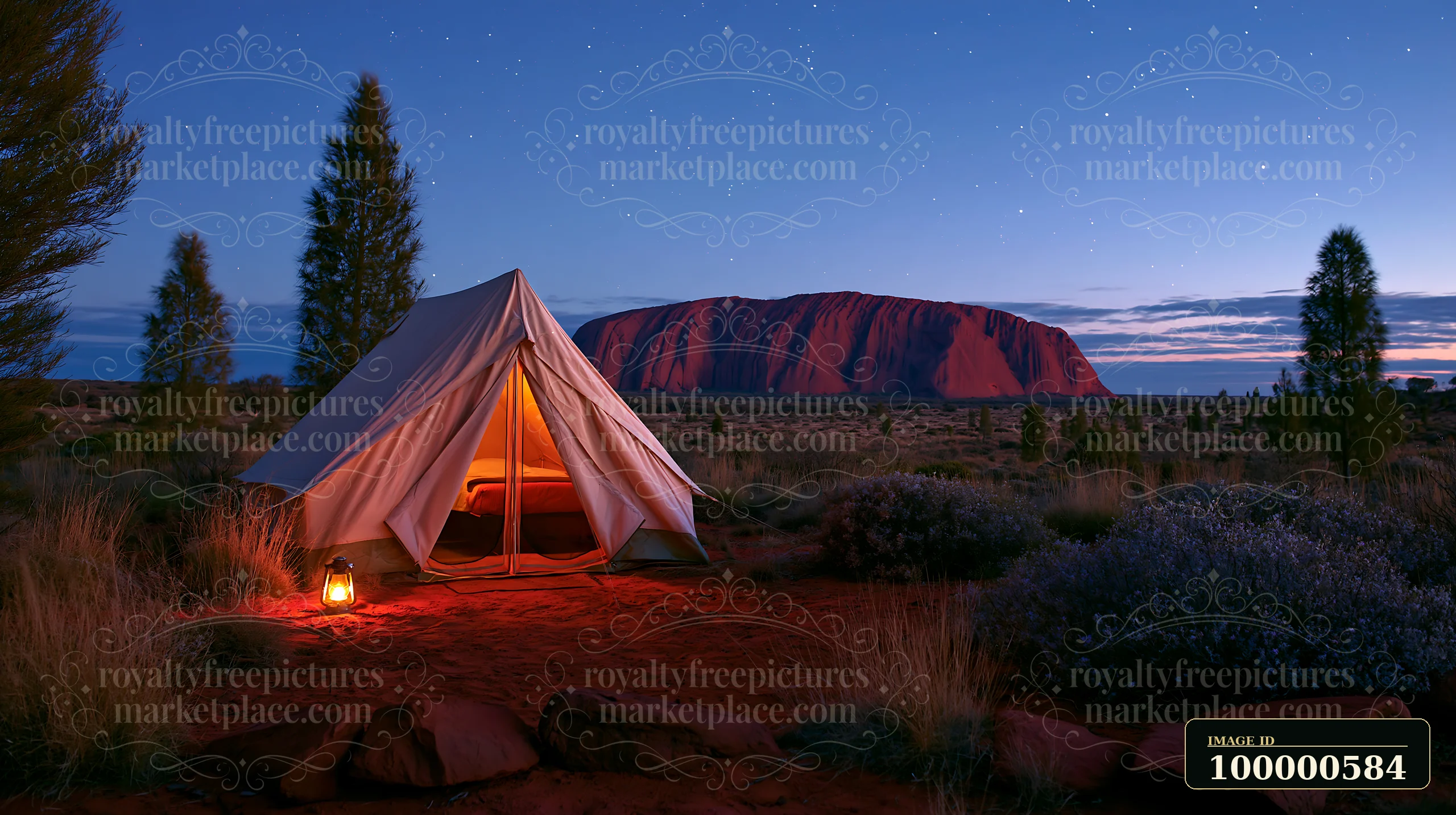A tent stands in the foreground with a lantern lit next to it under a starry sky and Uluru in the background.