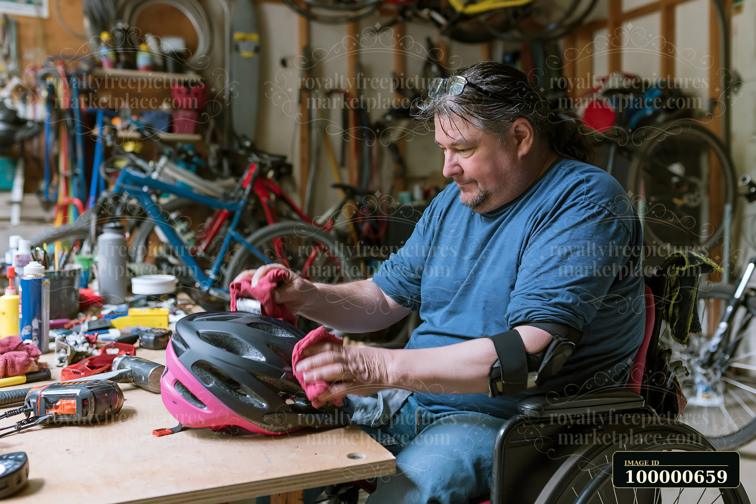 A man in a wheelchair is focused on cleaning a bicycle helmet with a cloth while surrounded by tools and bicycles in a garage workshop.