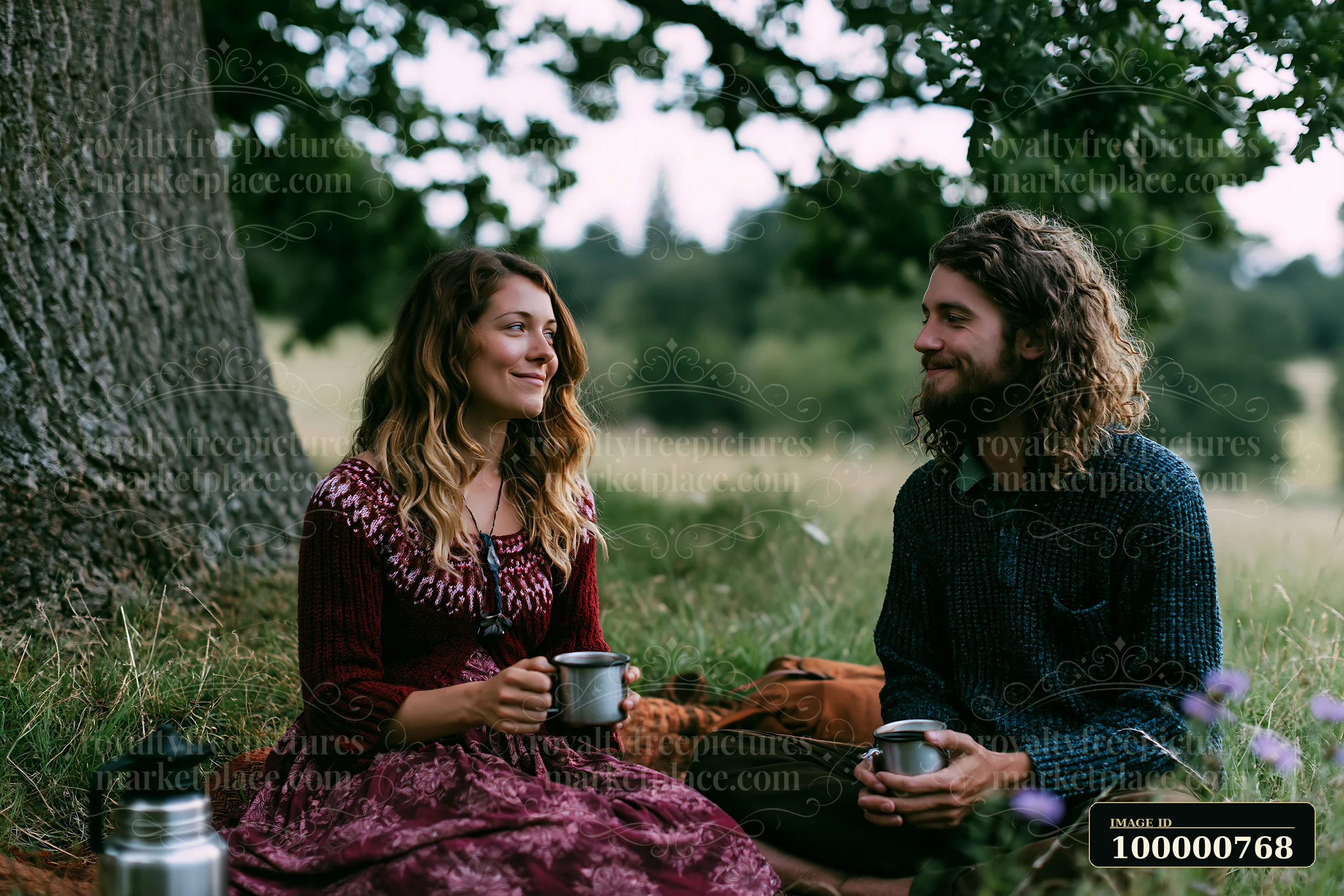 A couple sits on a blanket in a meadow beneath an oak tree, sharing drinks and smiles.
