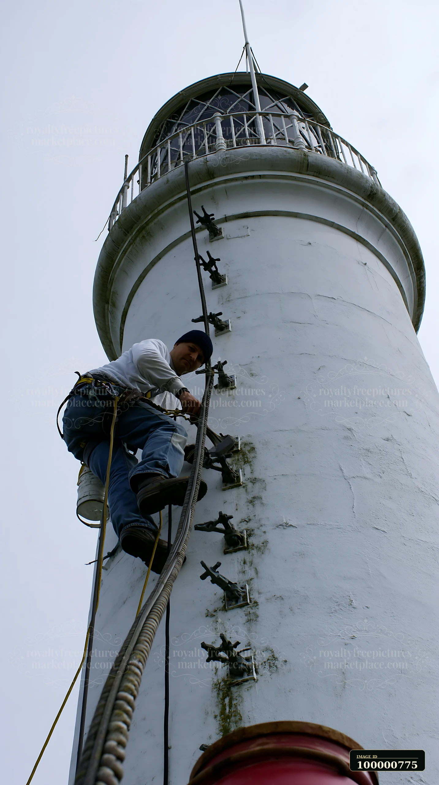 A lighthouse maintenance worker at work climbs the side of a tall lighthouse, focusing on repairs.