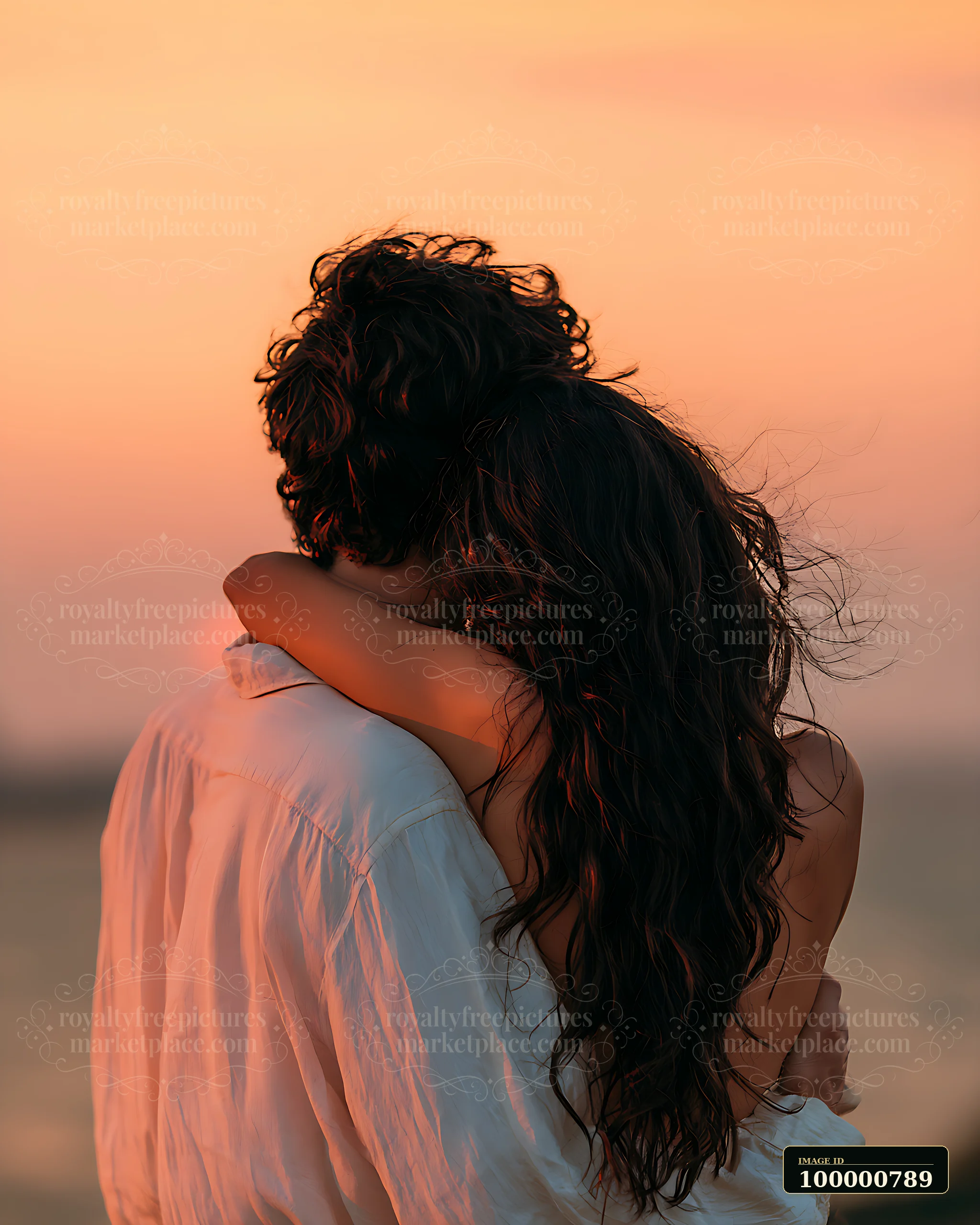 A couple stands together on the beach, holding each other close as the sun sets in the background, casting a warm glow over the scene.