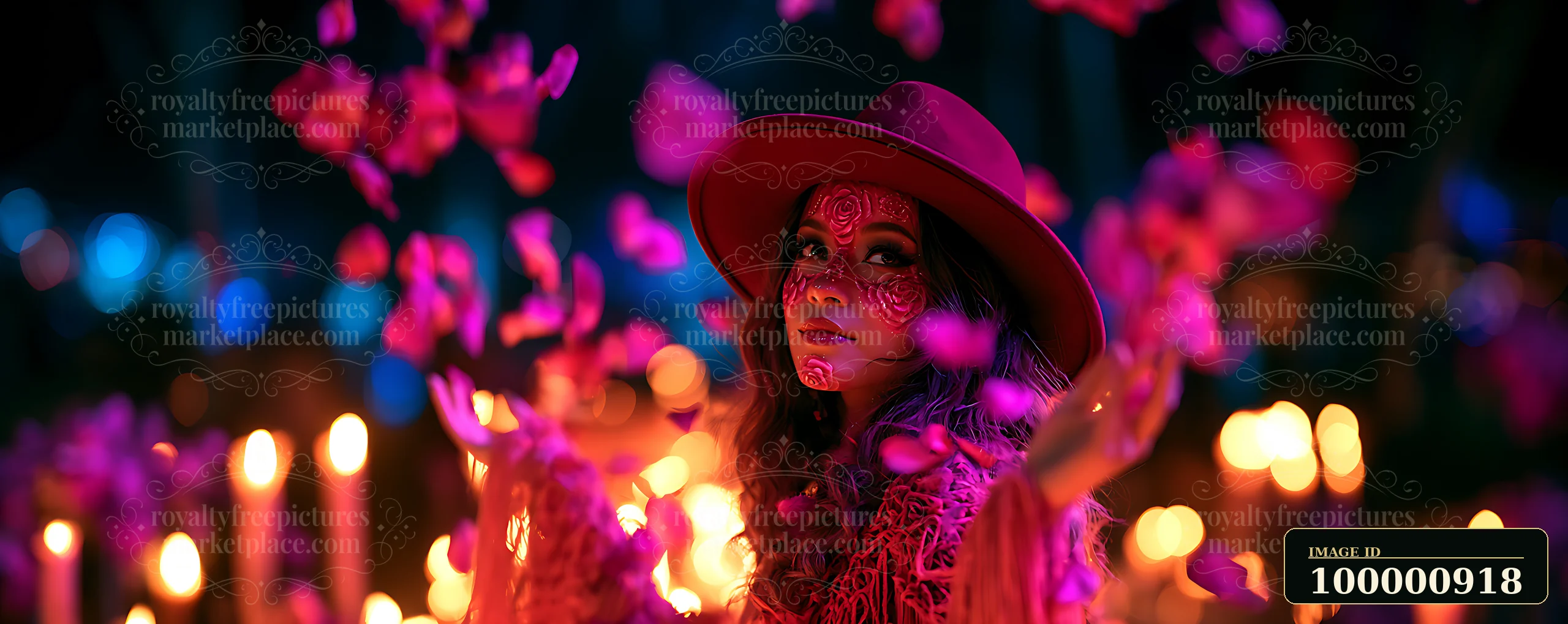 A woman wearing a wide-brimmed hat blows colorful flower petals into the air at a candlelit gathering.