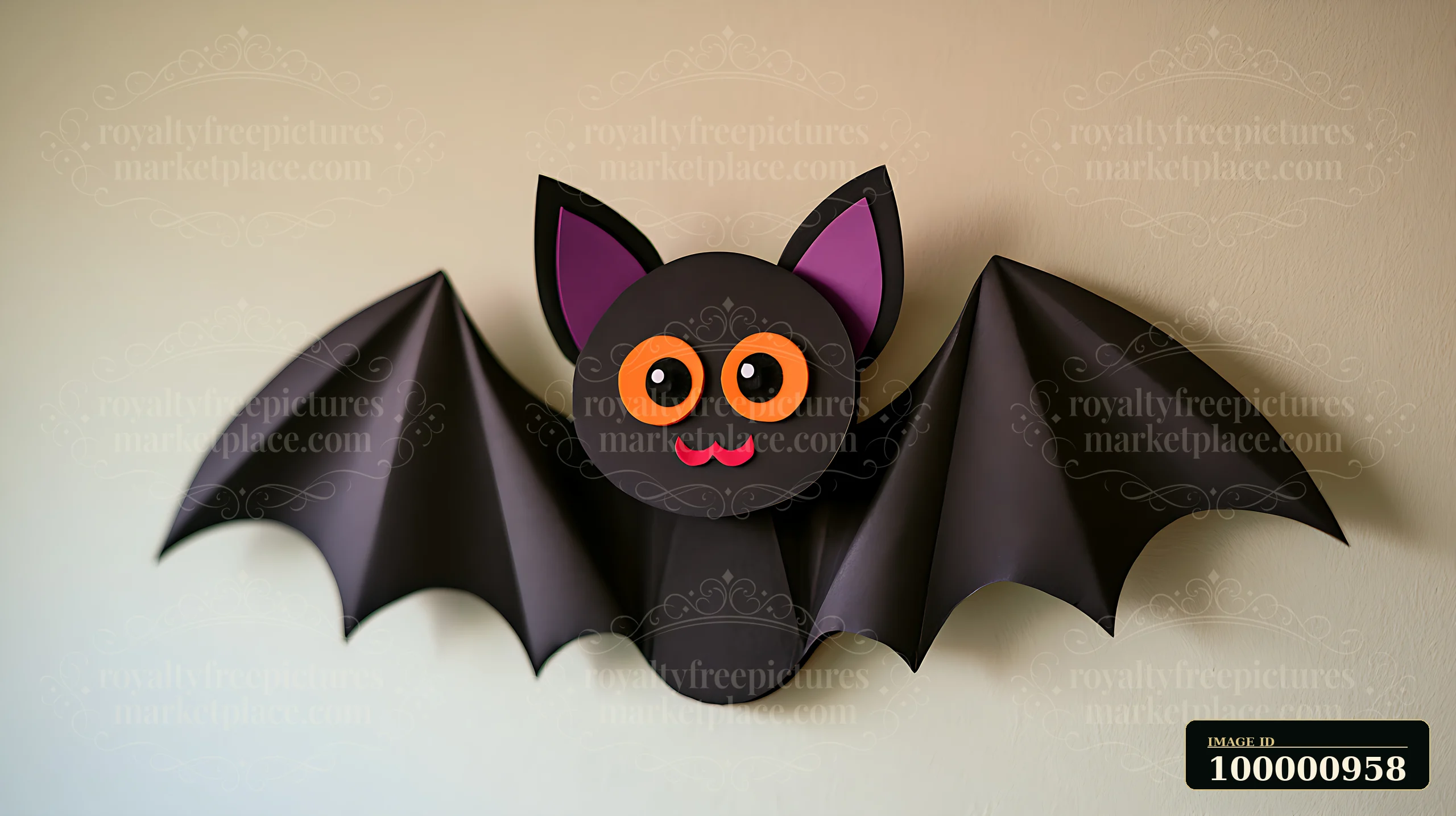 A black paper bat with large orange eyes and pink ears hangs on a light wall.