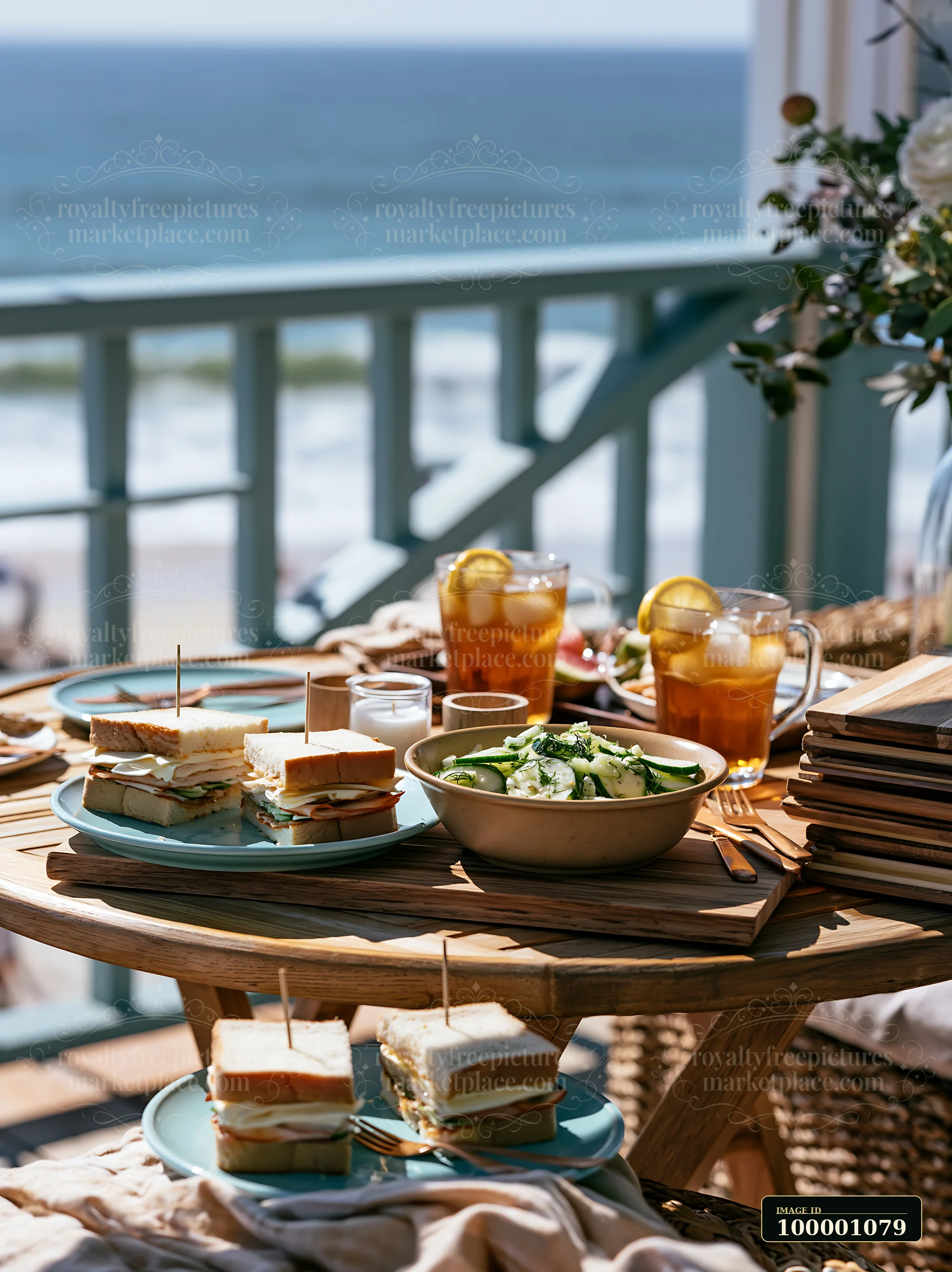 Friends gather for a beach picnic buffet featuring sandwiches, salad, and drinks on a table with an ocean view.