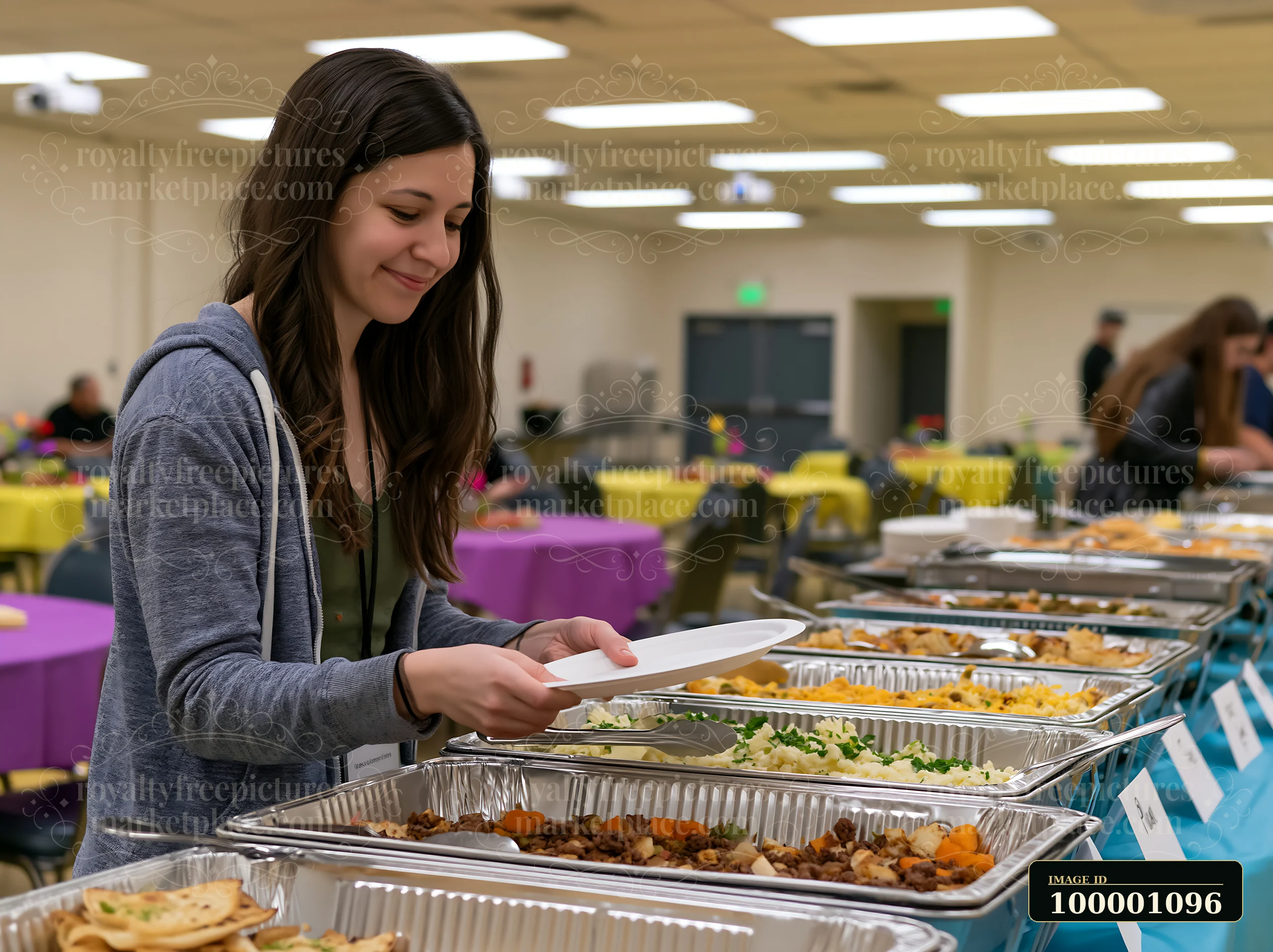 A woman selects food from a catering buffet setup at a large indoor event space.