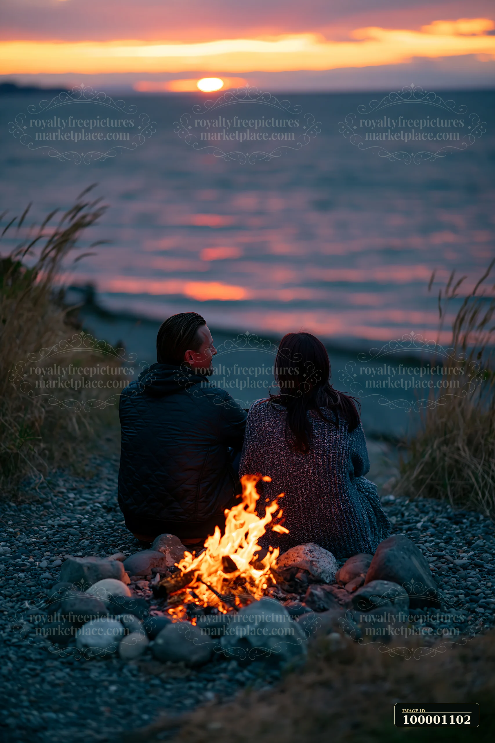 A couple enjoys a bonfire on the beach as the sun sets over the coastline with beach bonfire.