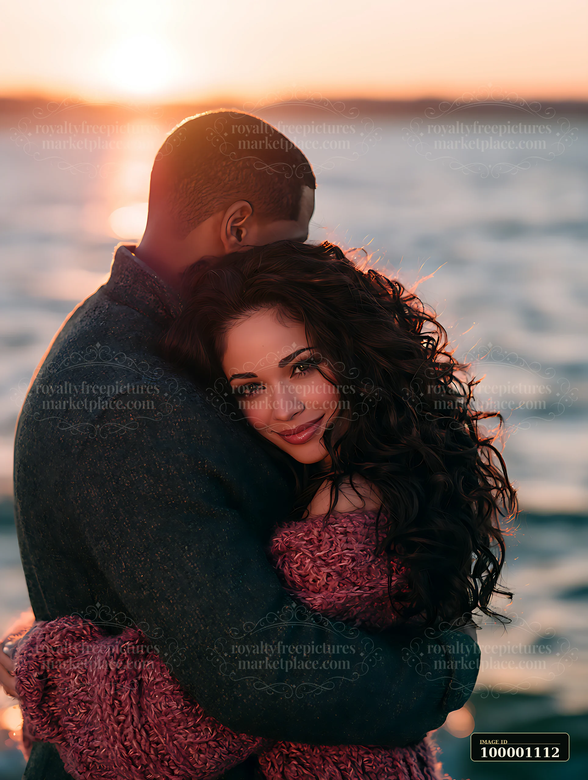A couple hugs closely near the water as the sun sets on the horizon.
