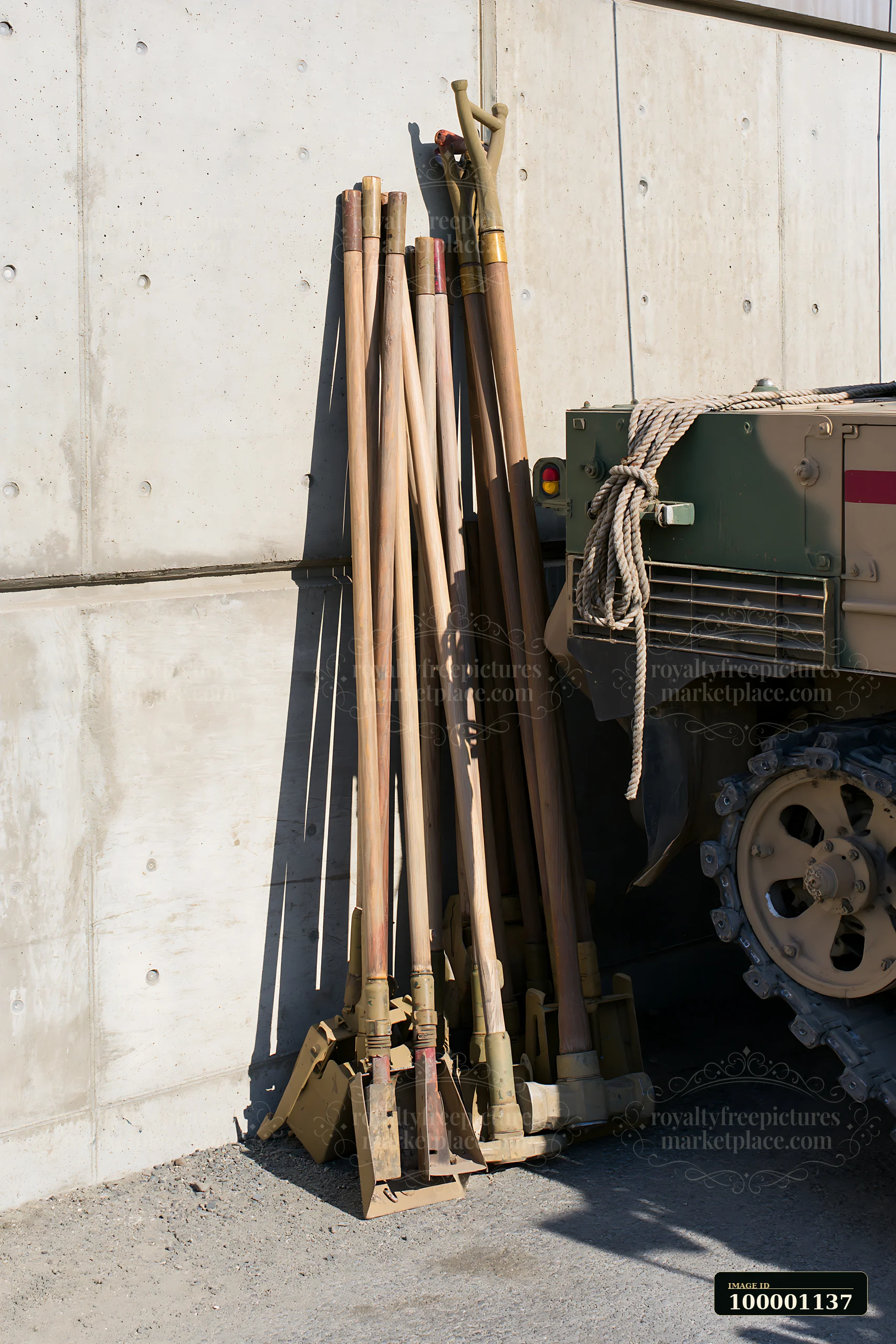 Various panzer tank maintenance tools are placed against a concrete wall next to a military vehicle.