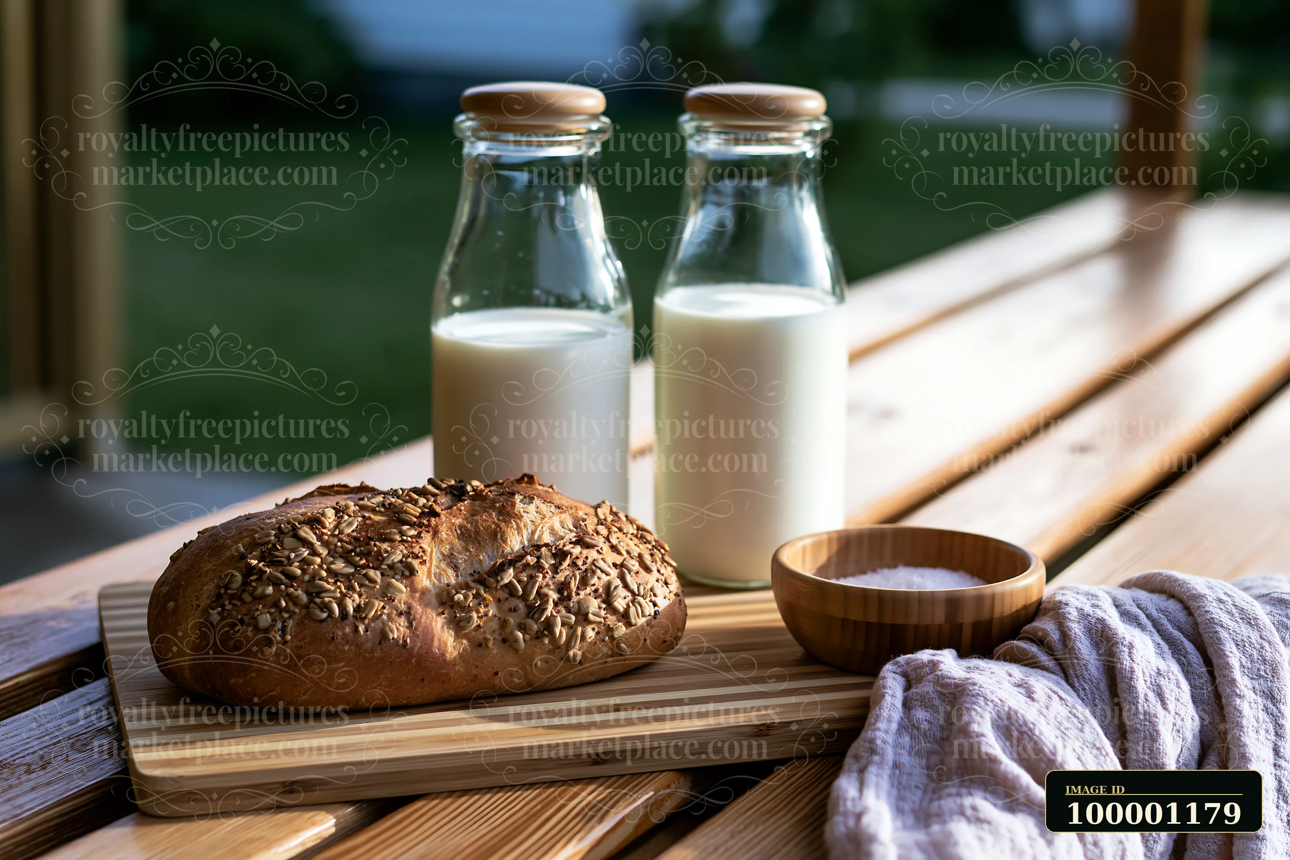 Glass milk bottles arranged beside fresh bread on a wooden table outdoors.