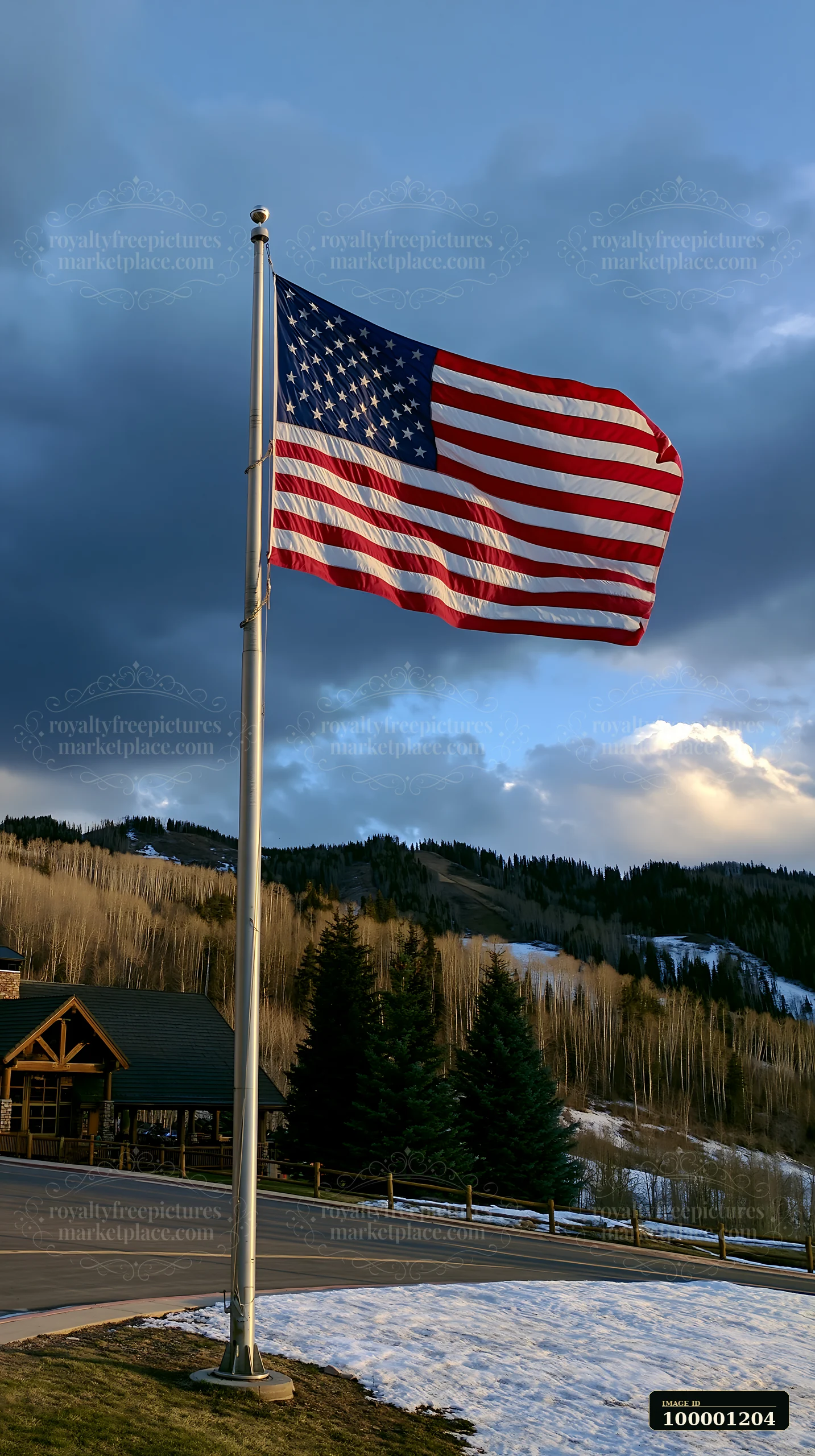 American flag flying in strong wind above a landscape with mountains and trees.