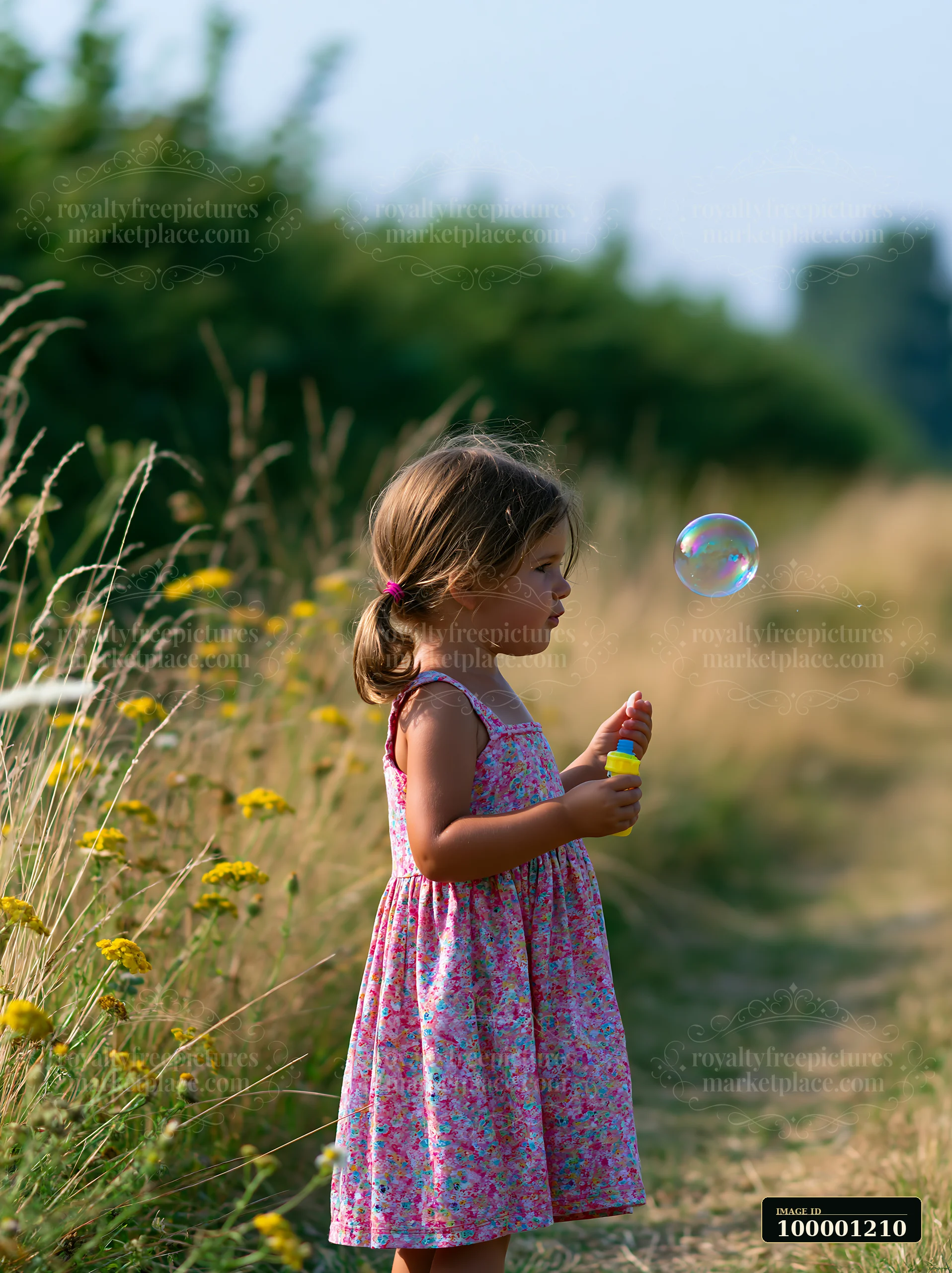 A child holds a bubble wand in a meadow surrounded by hedgerows.