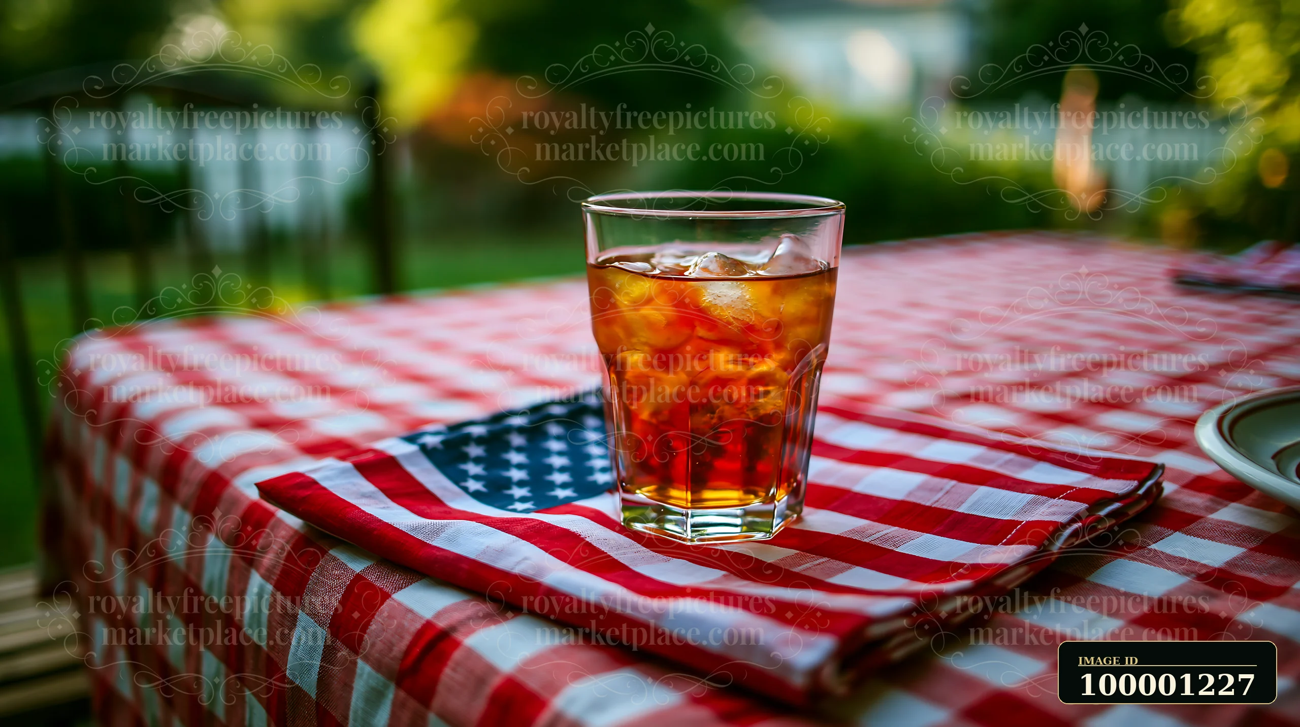 A glass with a beverage rests on an American flag table decoration next to a checkered tablecloth.