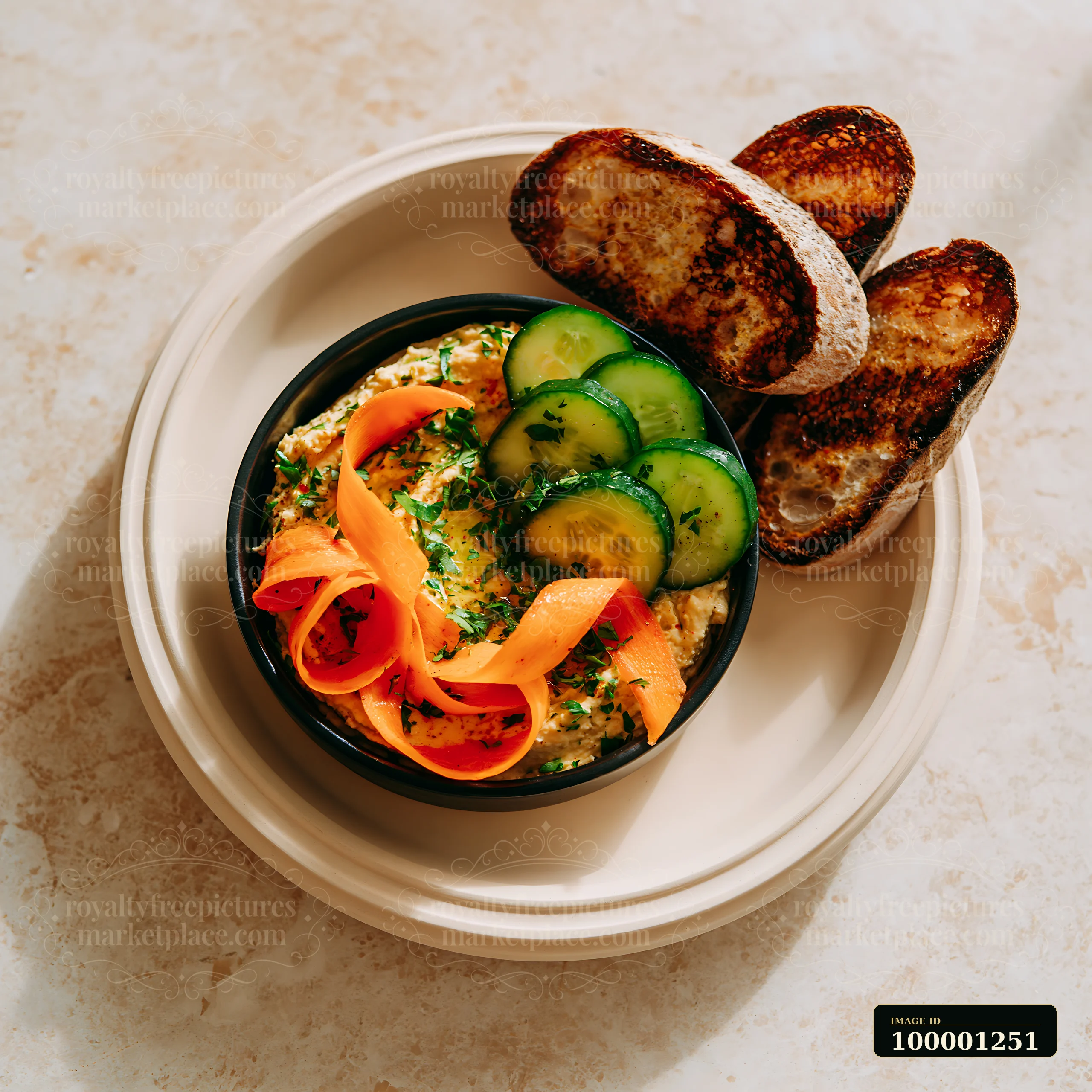 A breakfast plate with hummus includes fresh cucumber slices, carrot ribbons, and toasted bread.