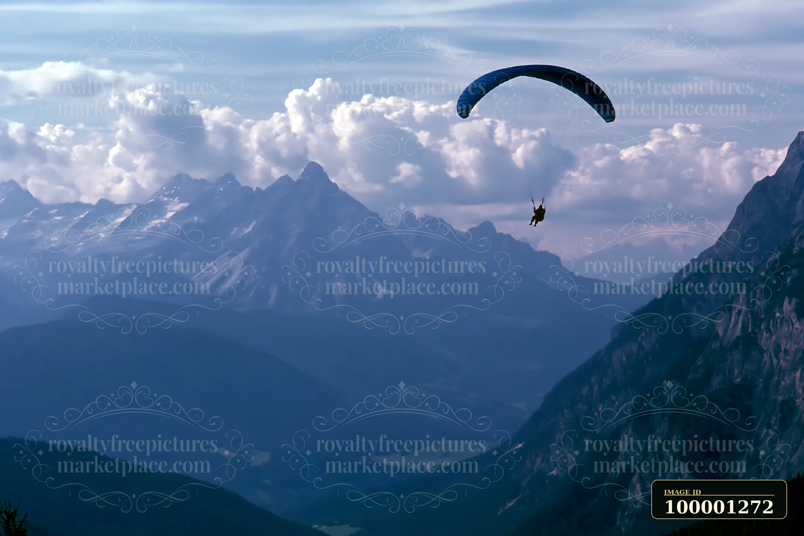 A person paraglides through the air with majestic mountain peaks and dramatic clouds around alpine peaks in the background.