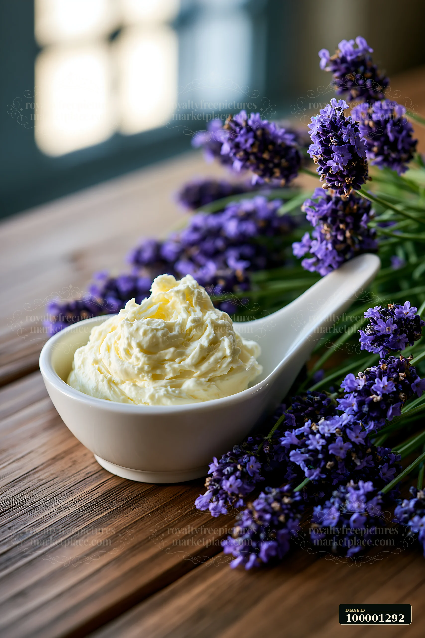 A bowl of cream sits on a wooden table with fresh lavender flowers nearby.