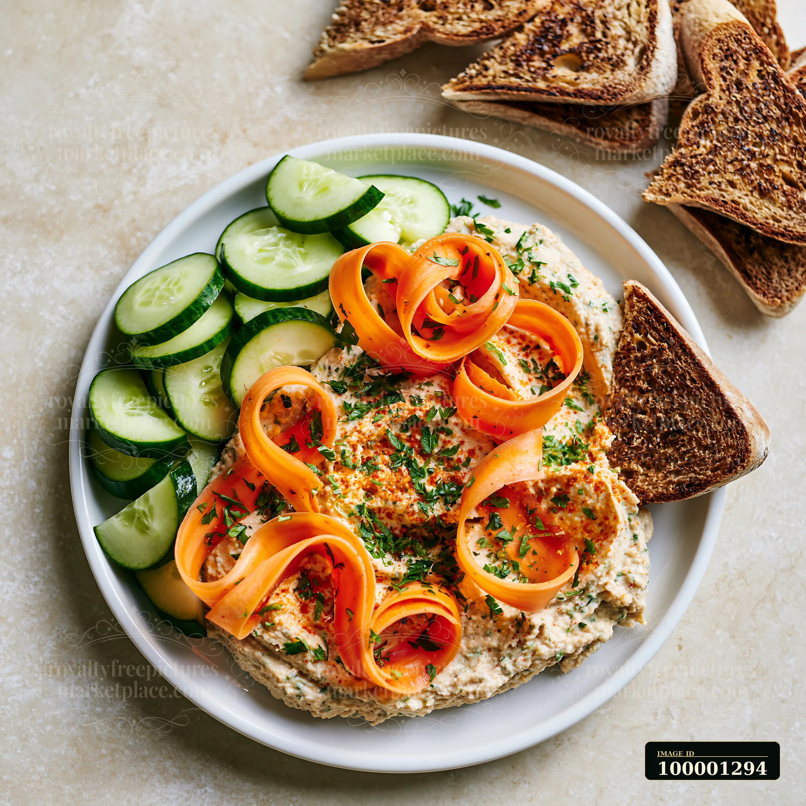 This plate features hummus topped with sliced carrots and herbs, surrounded by cucumber slices and toast.