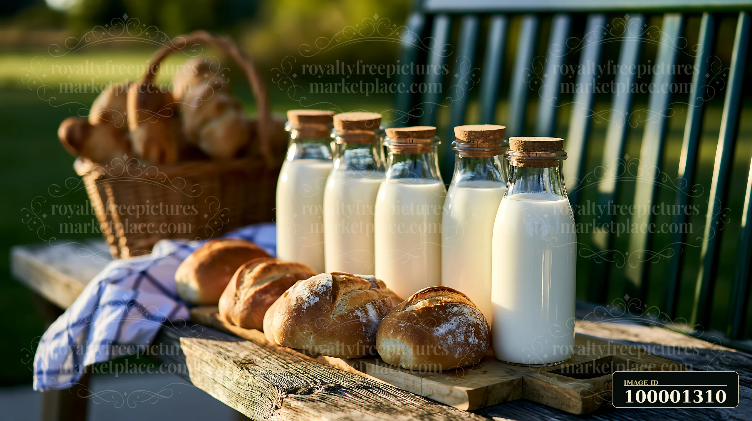 Glass milk bottles arranged beside fresh bread on a wooden bench create a simple setting in a sunny outdoor area.