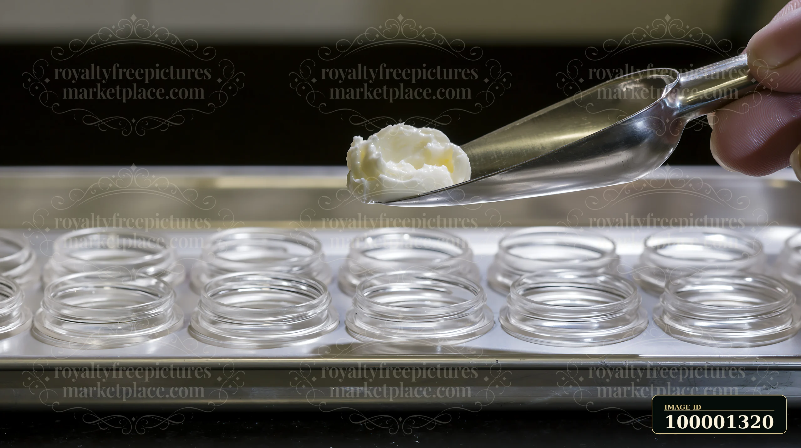 A person holds a cosmetic scoop filled with cream over a tray with multiple small glass jars.