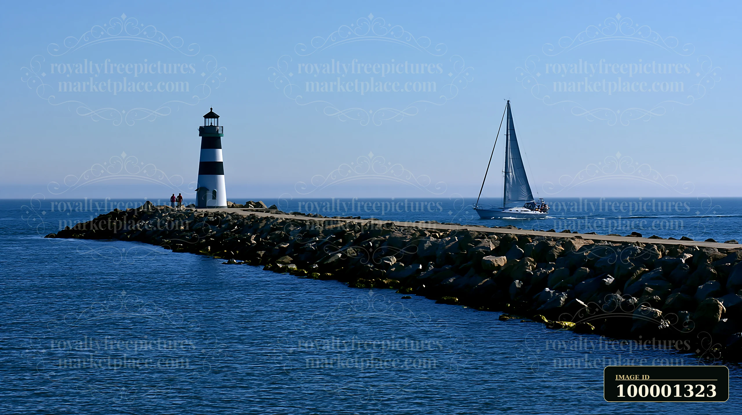 A lighthouse with black and white stripes stands at the end of a jetty while a sailboat approaches it under a clear blue sky.