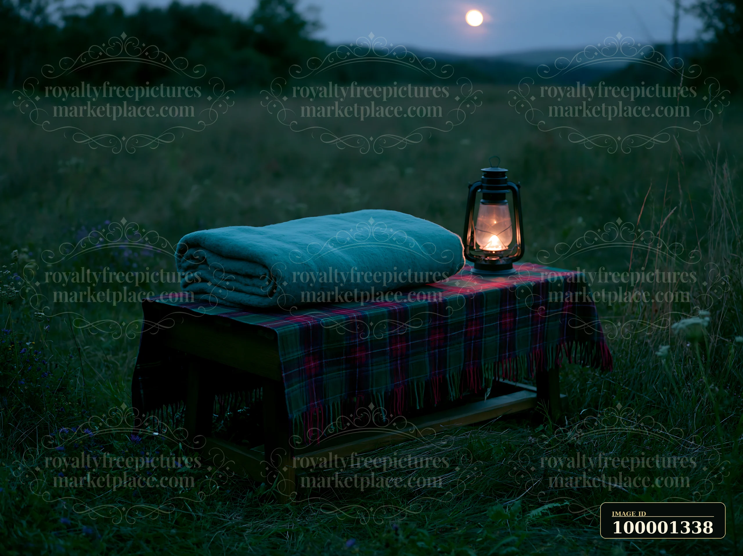 A cozy setup with a folded blue blanket on a wooden table and a lantern glowing in a meadow beneath a full moon.