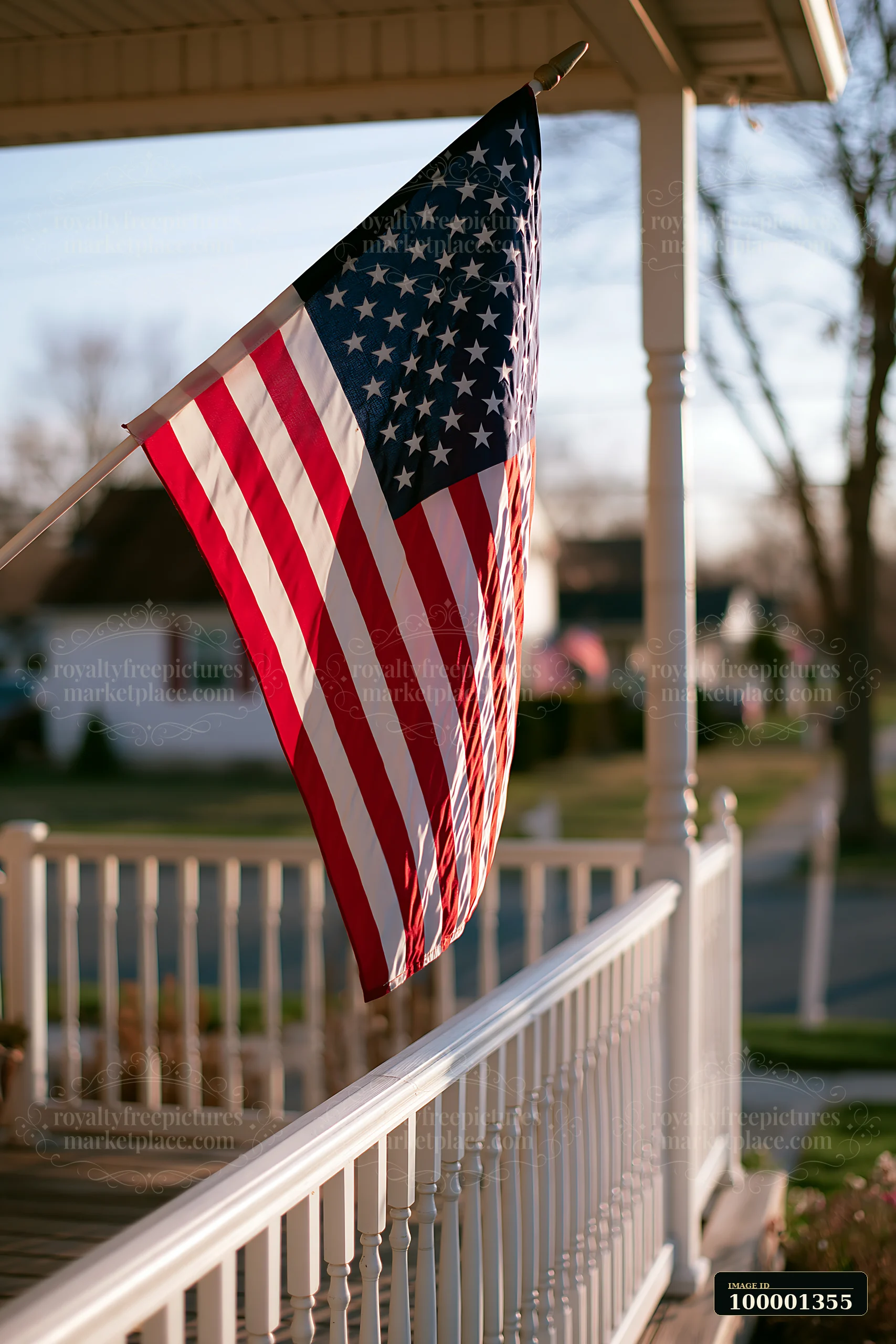 The American flag flies proudly in strong wind on a porch, with the sun setting in the background.