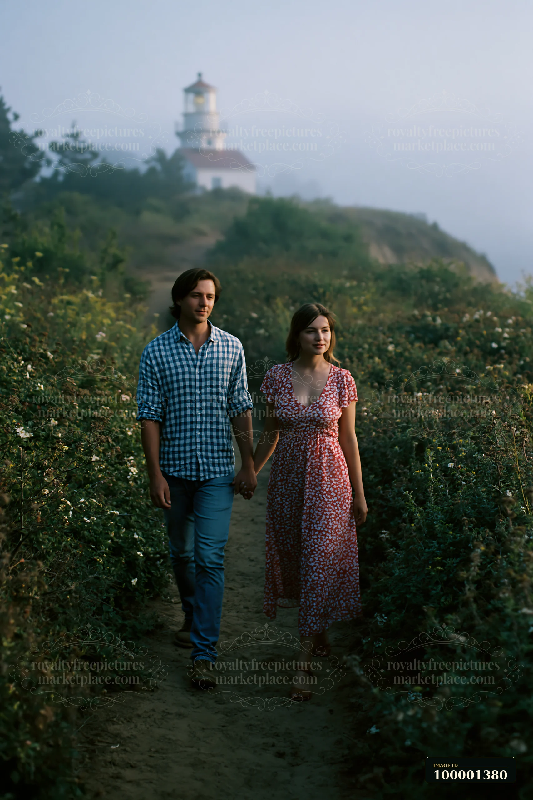 A couple walks hand in hand along a coastal path, exploring the area near a lighthouse with fog covering the landscape.