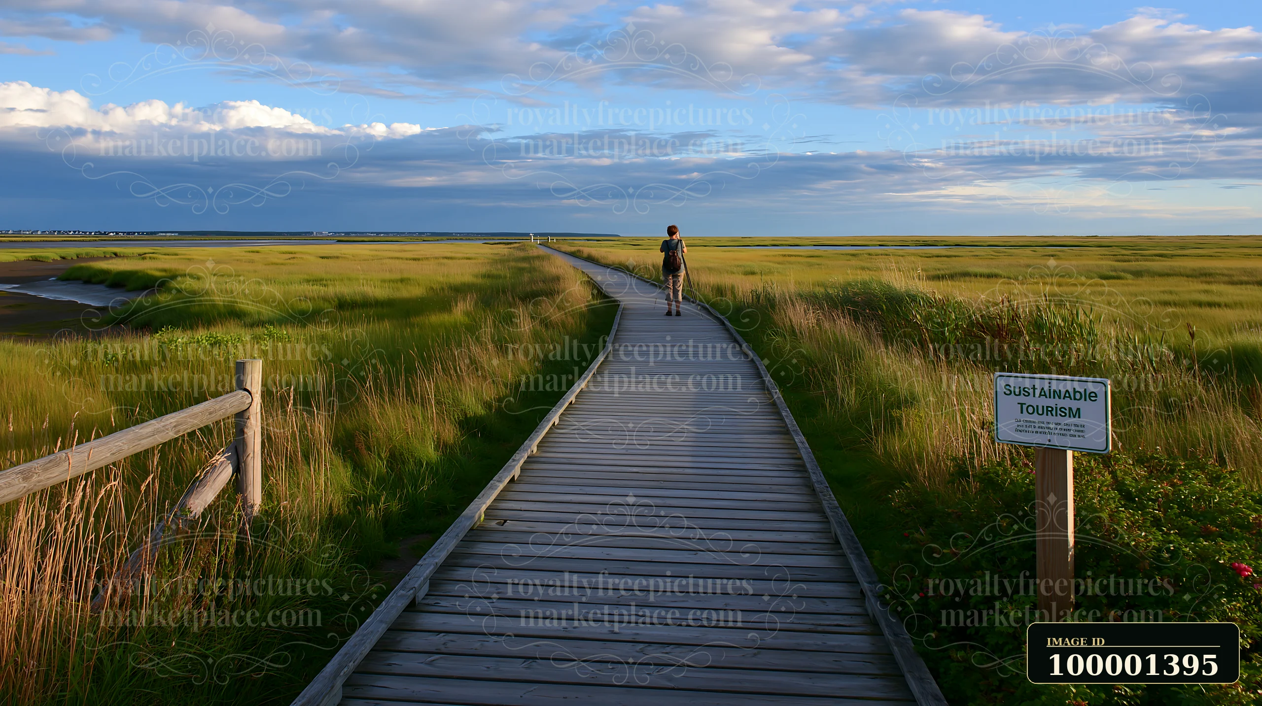 A person walks along a wooden boardwalk in a coastal area.