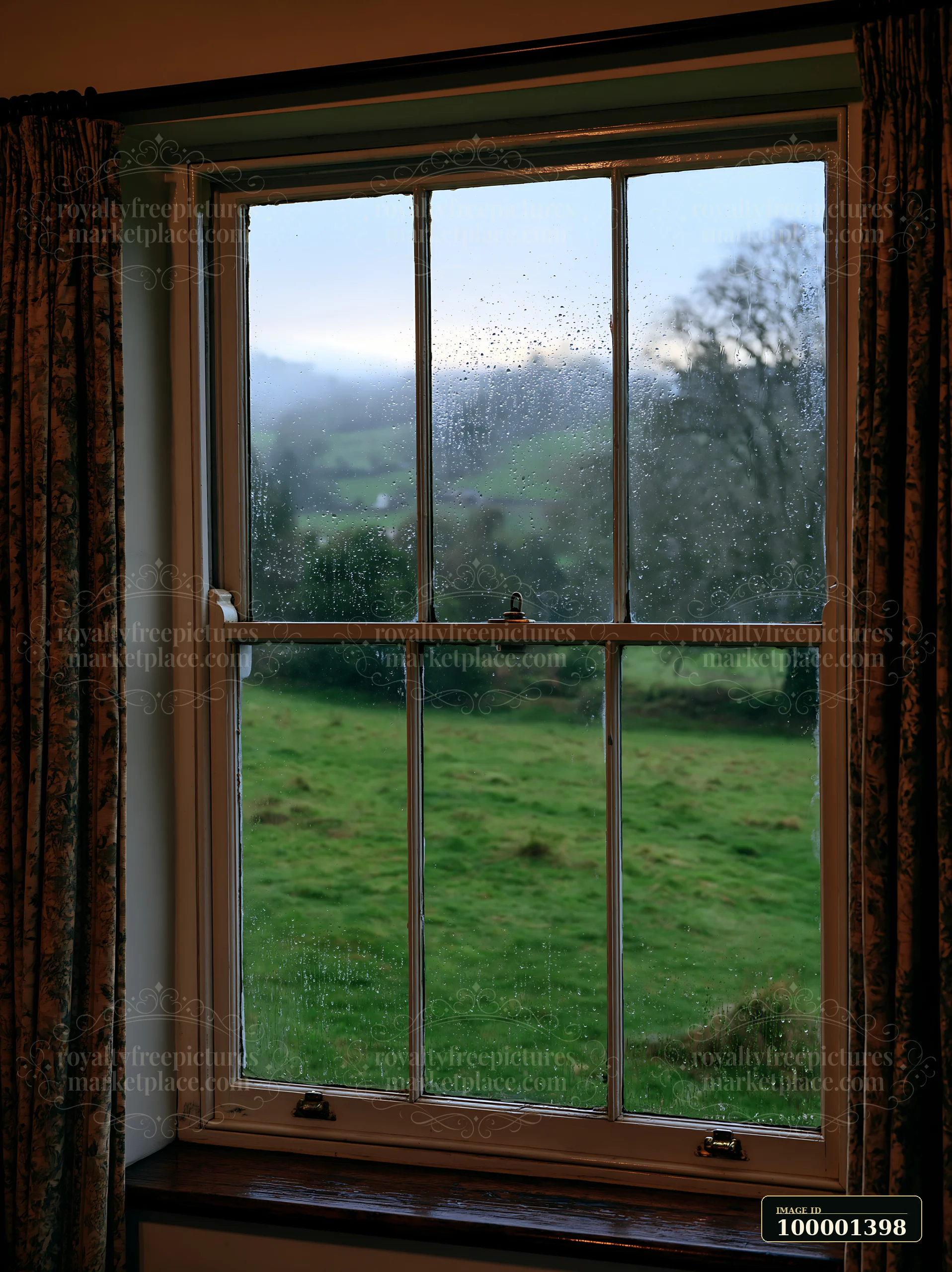 Raindrops cling to the window pane as a view of green fields and distant hills unfolds.