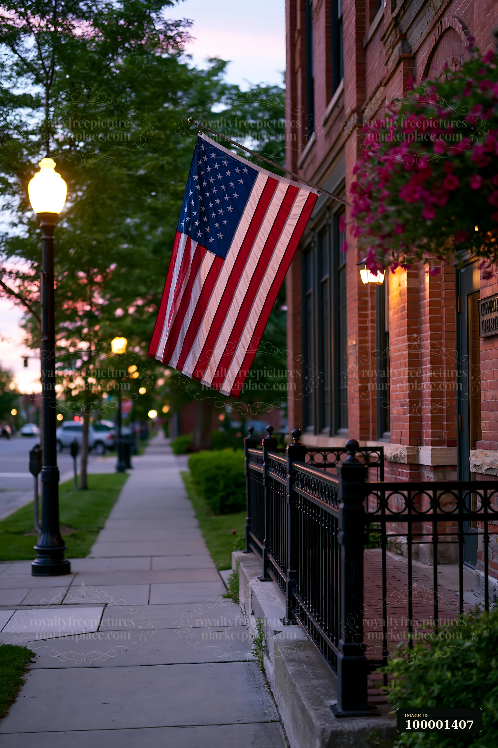 The American flag hanging vertically is displayed from a building near a sidewalk with street lamps.