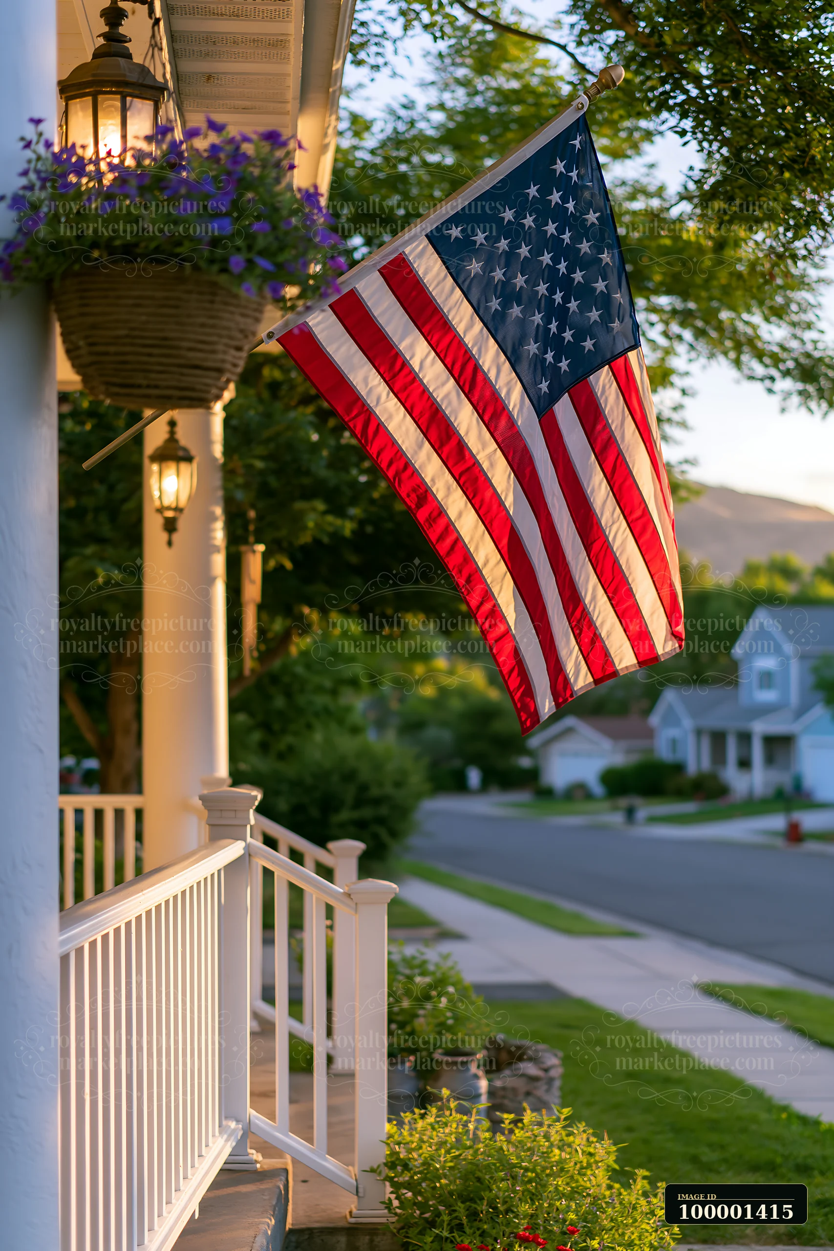 An American flag flying in strong wind on a porch near a quiet residential street.