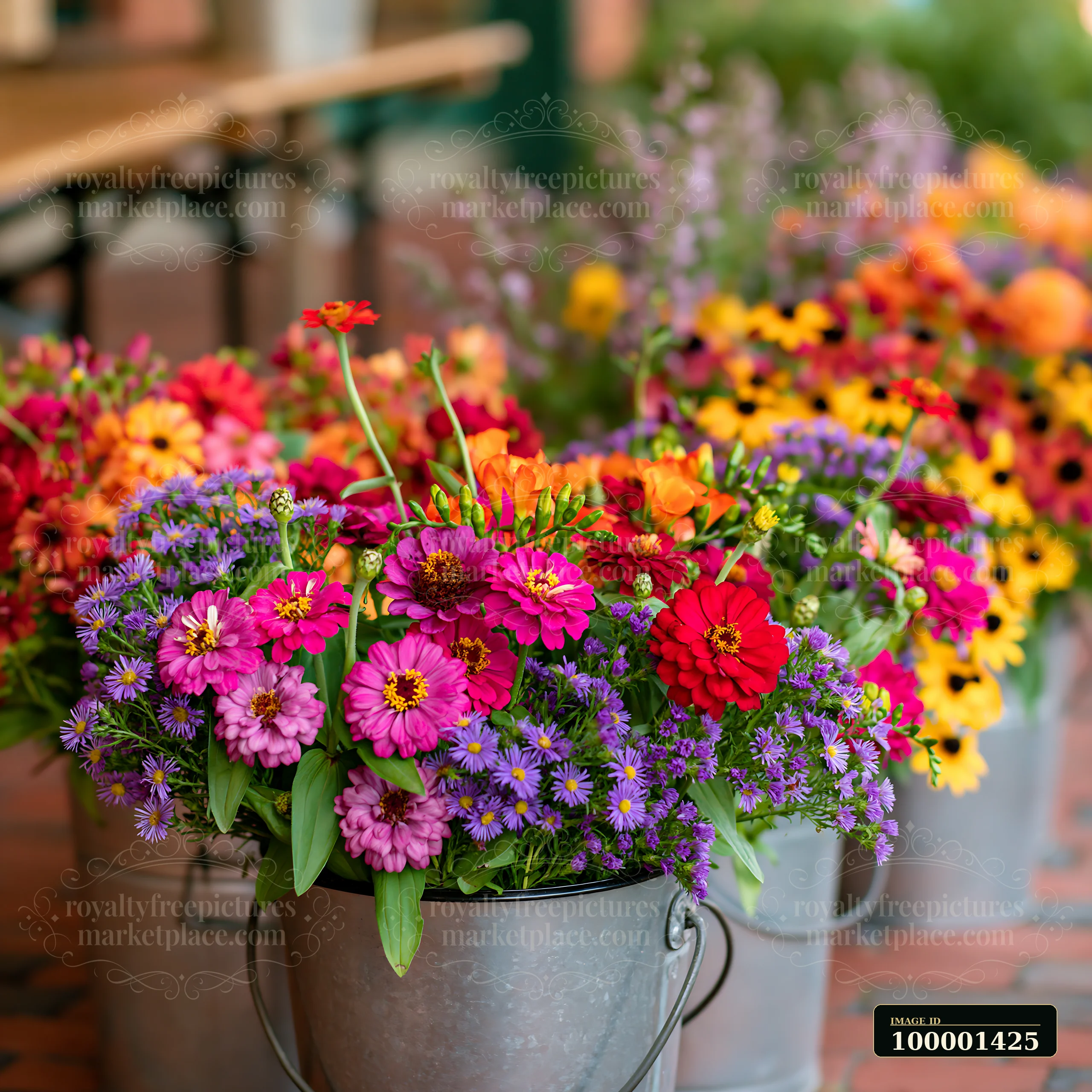Brightly colored mixed seasonal flowers in metal buckets are displayed at a farmers market.