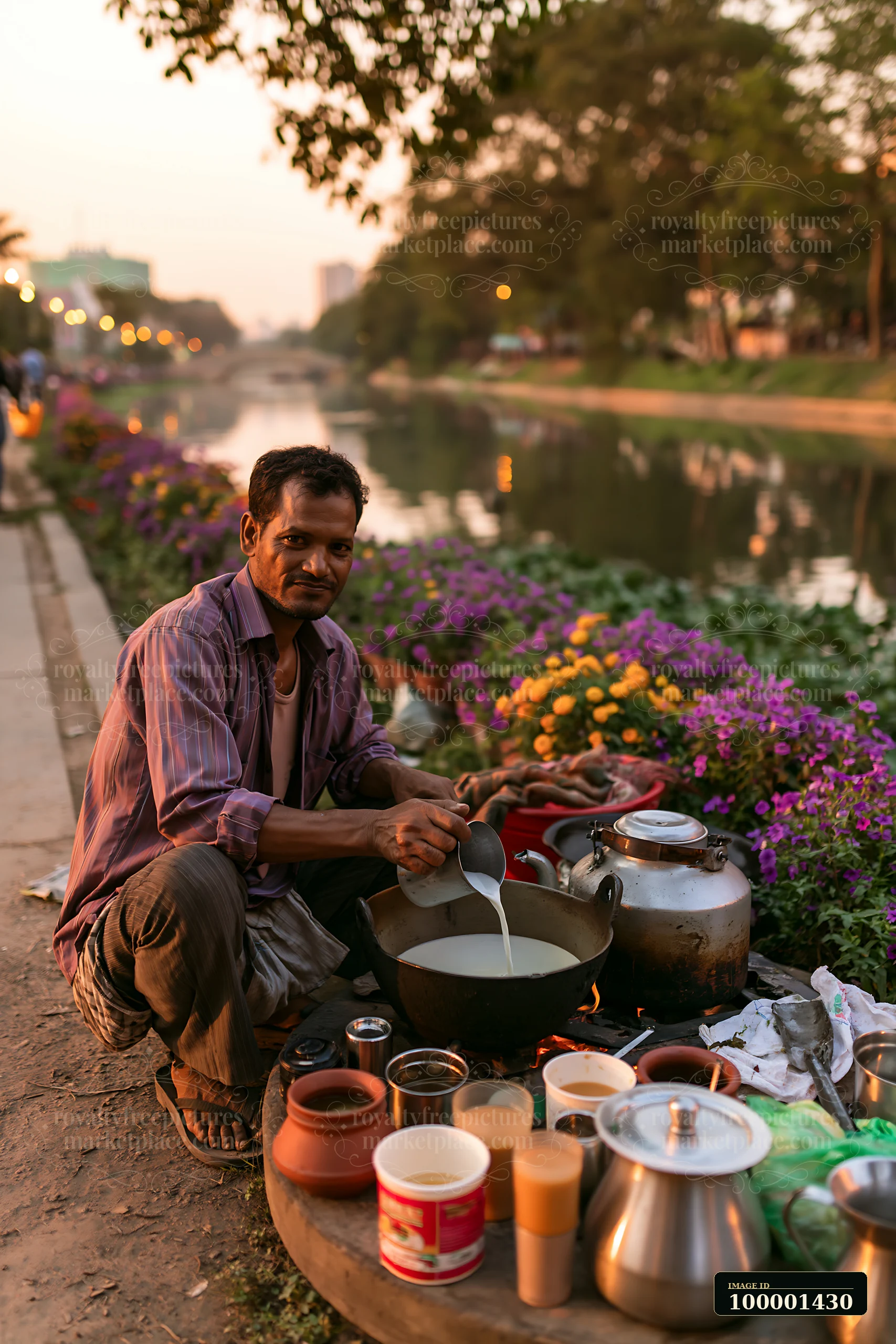A street food vendor adding milk to tea by the river during evening.