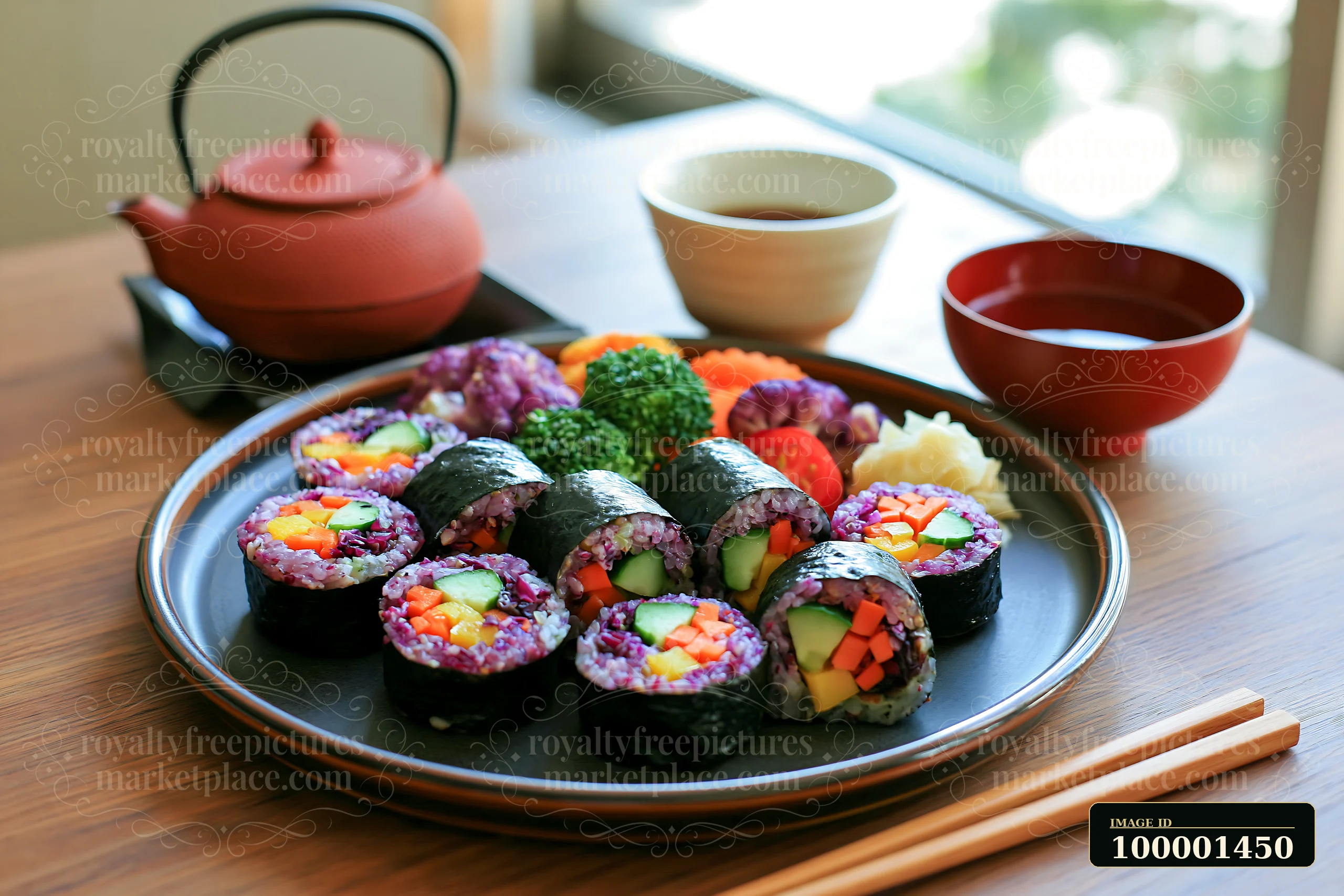 A plate of sushi featuring colorful rolls sits on a wooden table beside a teapot and cups.
