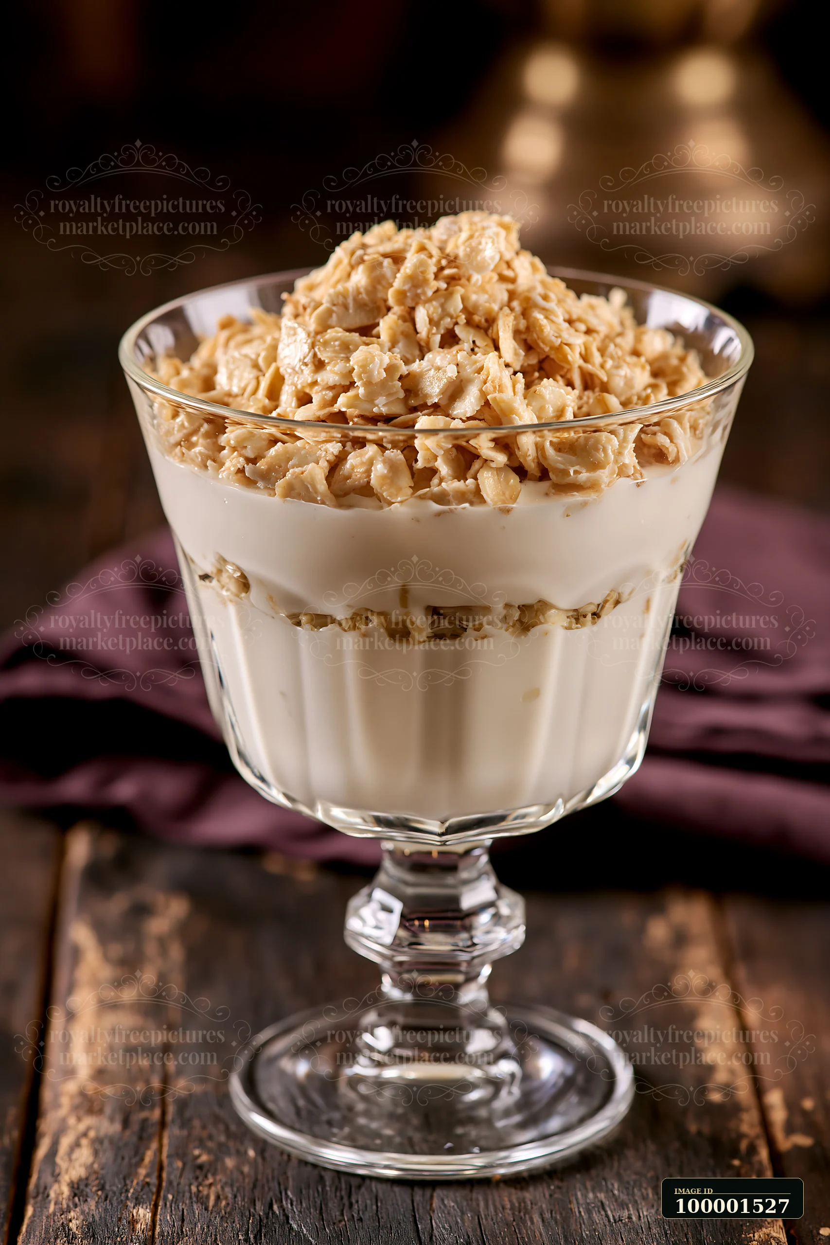 A glass cup holds a layered dessert made with cream and oat flakes, sitting on a rustic wooden table.
