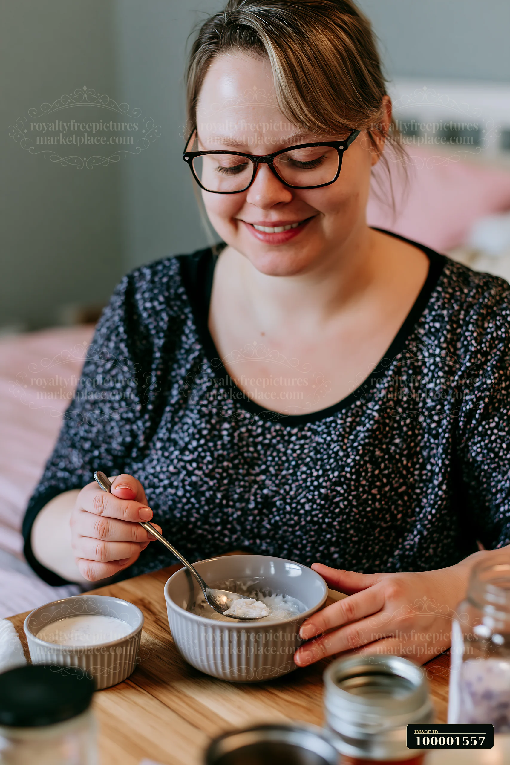 A person with limited hand mobility using utensils sits at a table smiling while eating from a bowl.