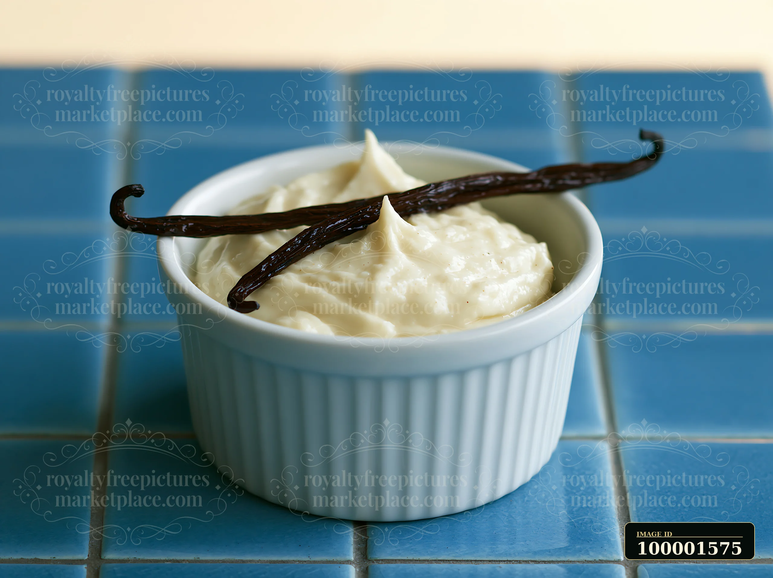 A bowl holds a creamy mixture topped with vanilla pods, placed on a blue tiled surface.