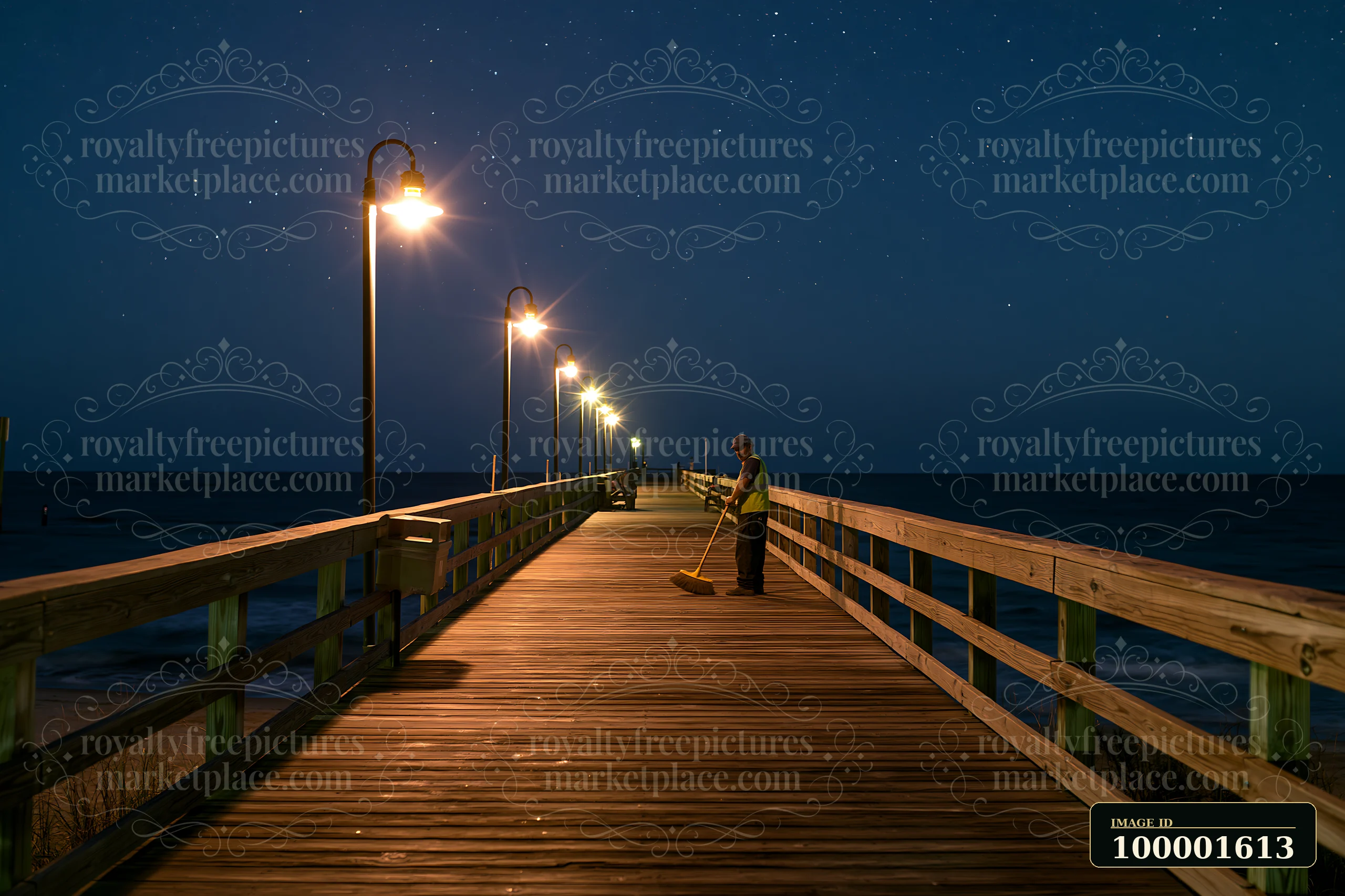 A worker sweeps the wooden boardwalk under bright lights while a starry night sky hangs above the ocean.