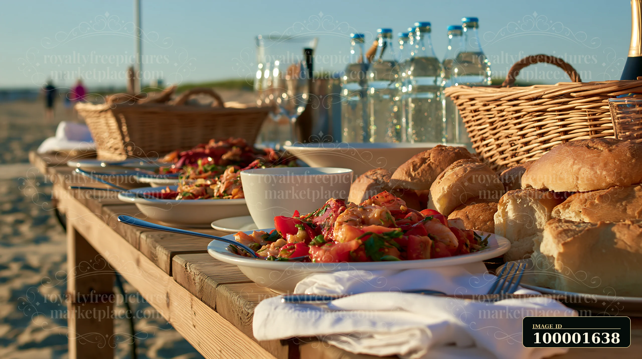 A beach picnic buffet features fresh seafood dishes, rolls, and beverages on a wooden table by the ocean during sunset.