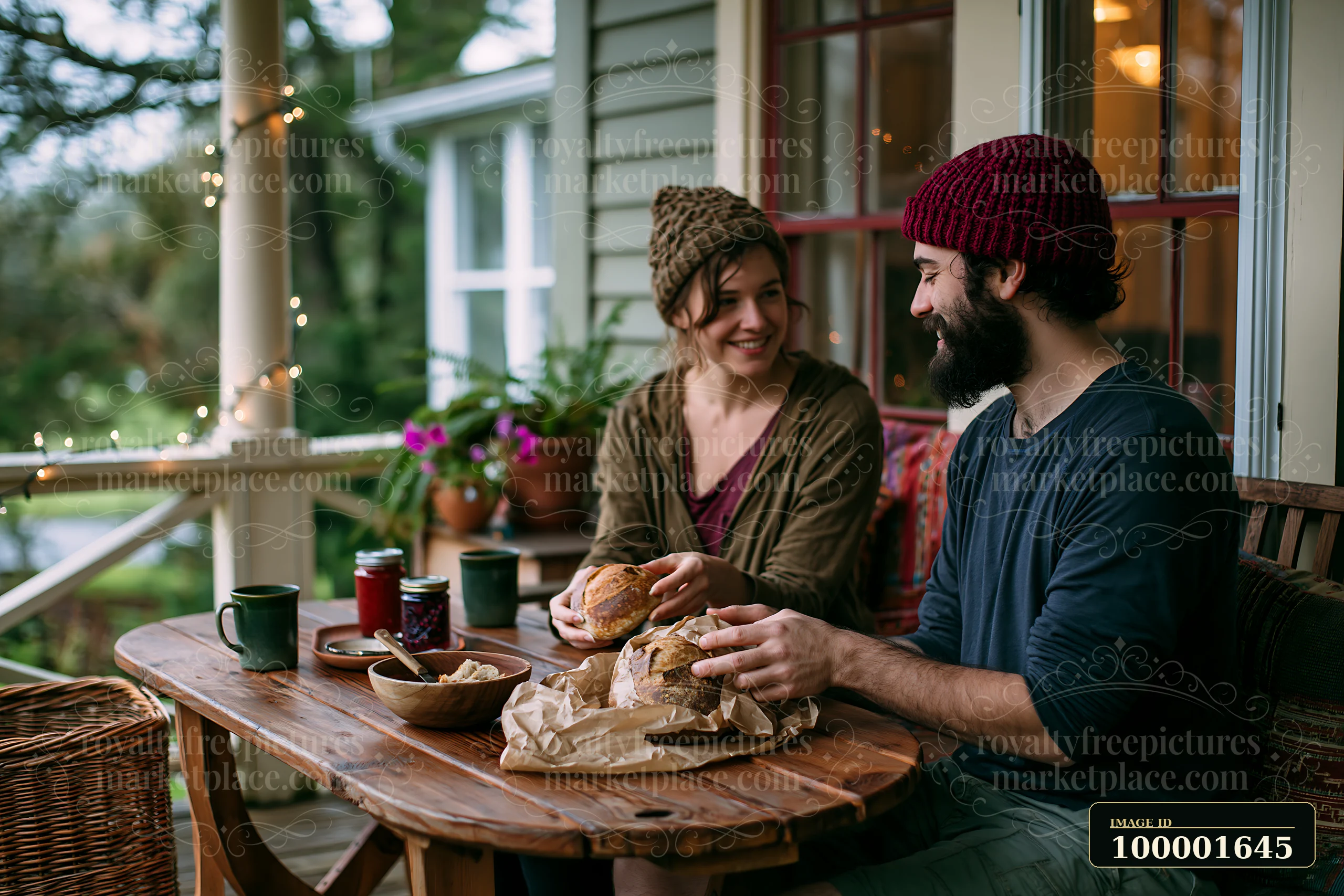 A couple on cottage porch enjoys a meal together on a wooden table with sandwiches and drinks.