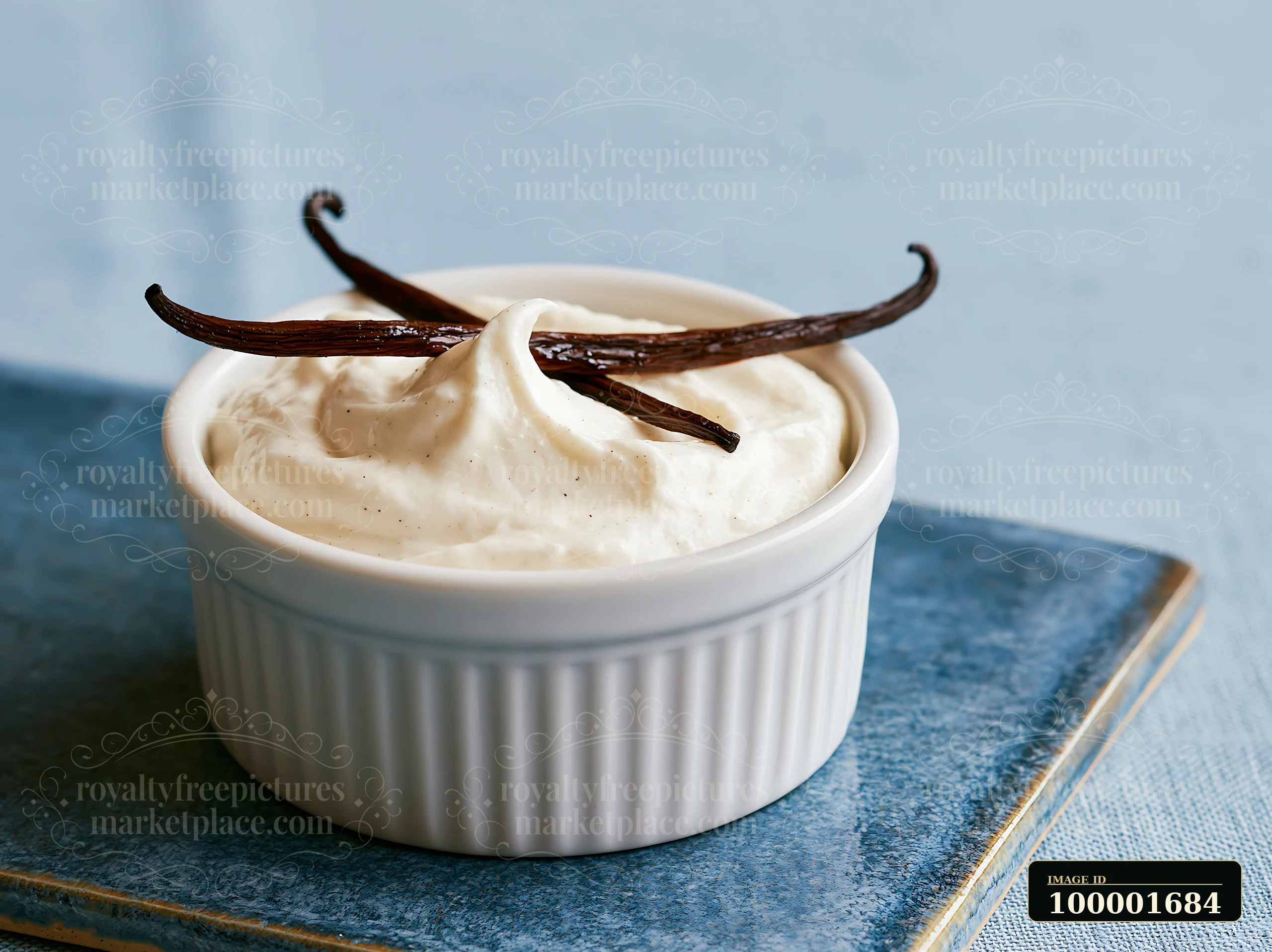 A small white bowl holds a creamy mixture topped with vanilla pods, set on a blue textured surface.